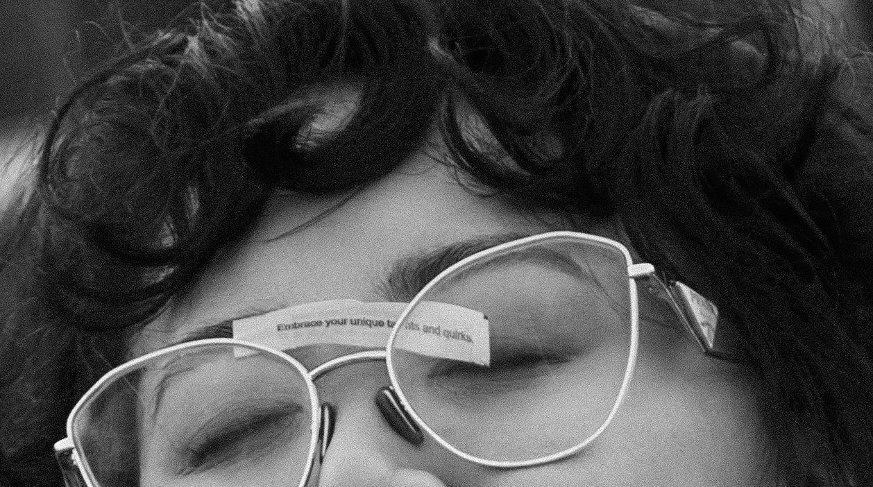 Black and white close-up of a woman with curly hair wearing clear-framed glasses with eyes closed.