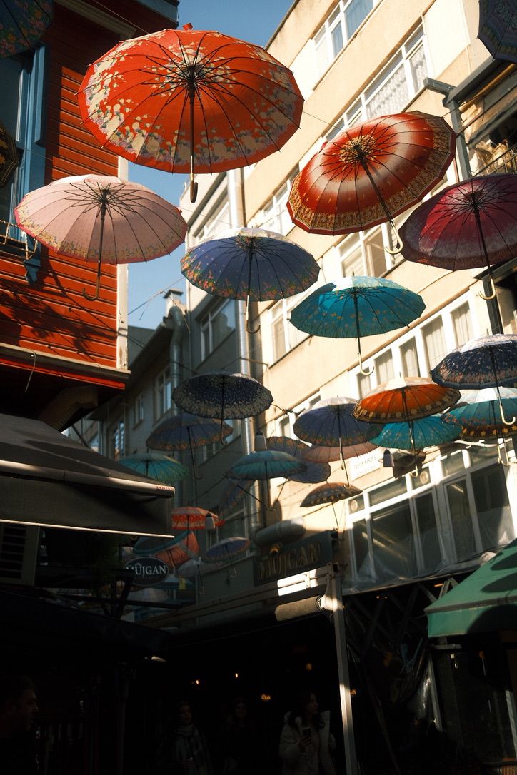 Colorful decorative umbrellas hanging over a narrow street between buildings in a vibrant outdoor market.