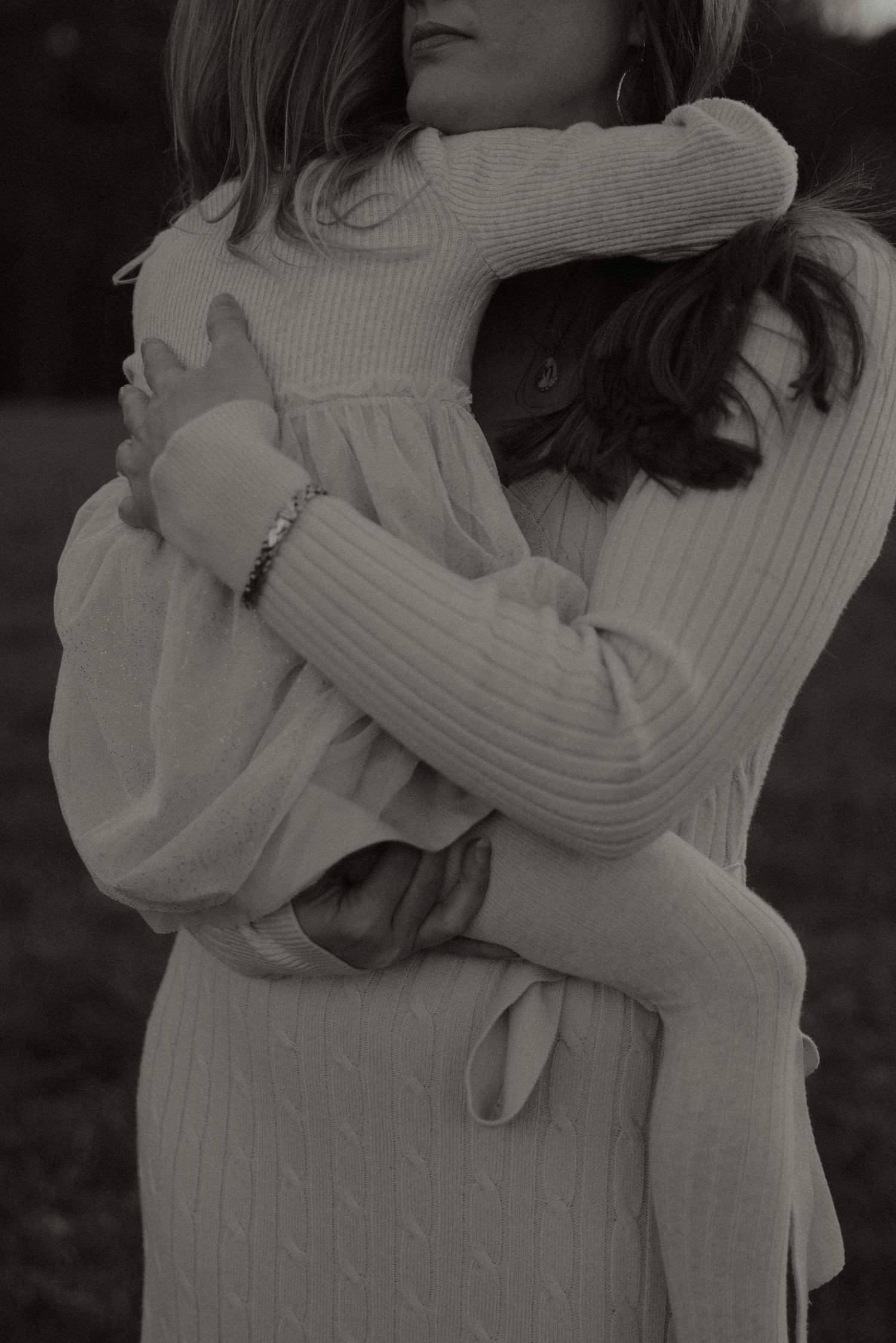 Black and white photo of two people sharing a warm embrace outdoors, wearing cozy knit sweaters.