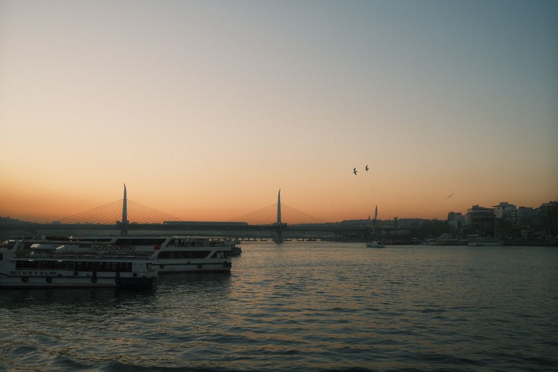 Serene Istanbul sunset over the Bosphorus with ferry boats and mosque minarets silhouetted on the horizon.