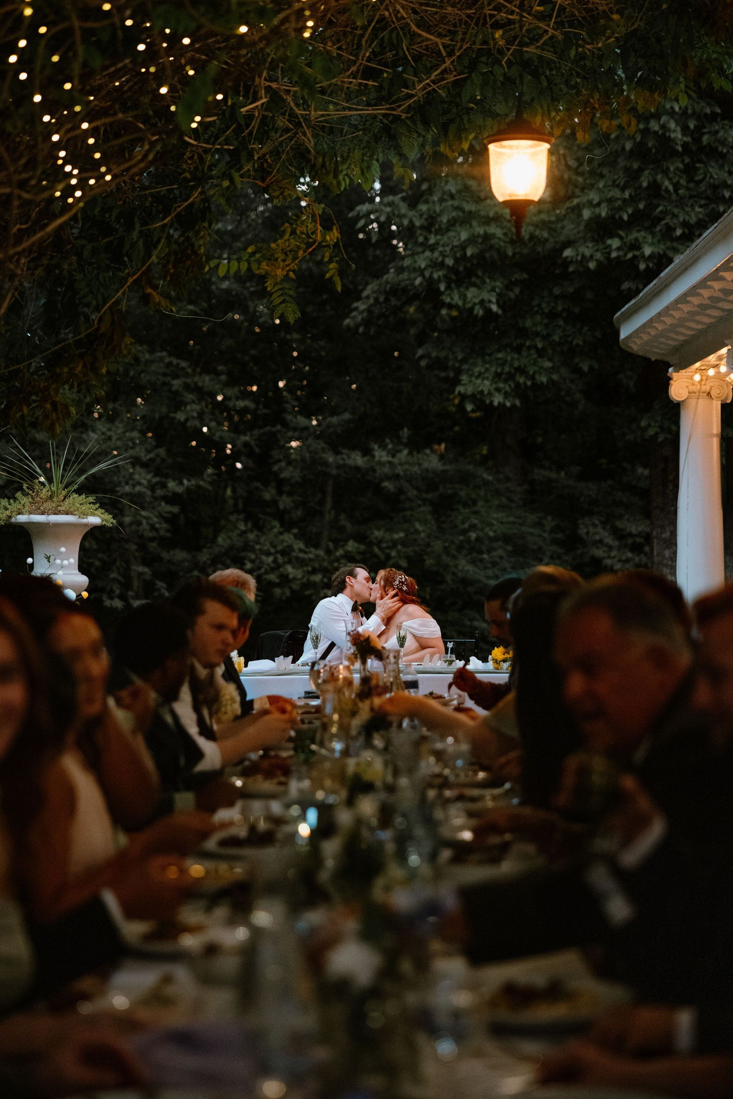 Couple sharing a kiss at their reception table during an enchanting outdoor evening dinner.