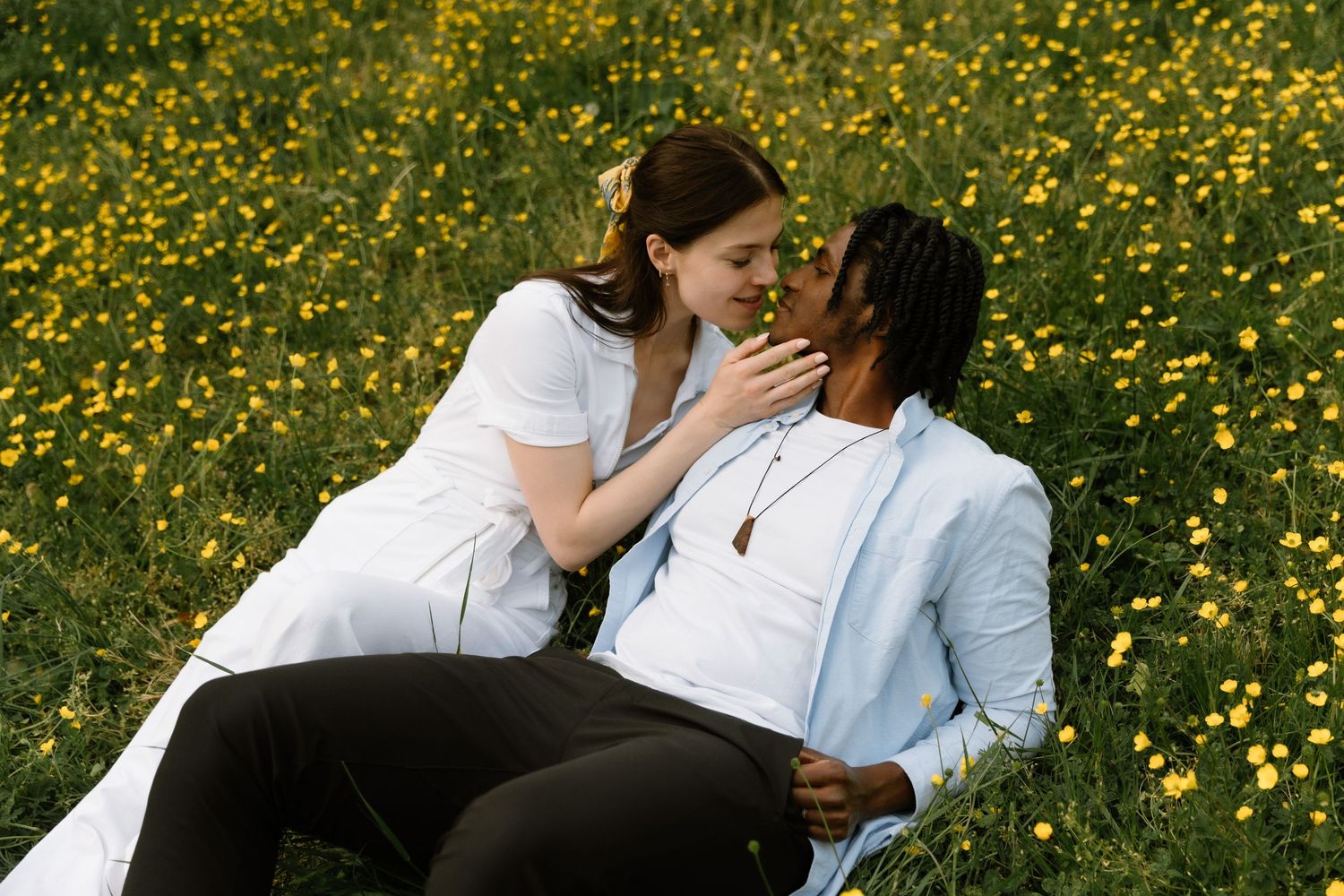 Romantic interracial couple sharing a tender moment sitting in a field of yellow wildflowers on a sunny day.