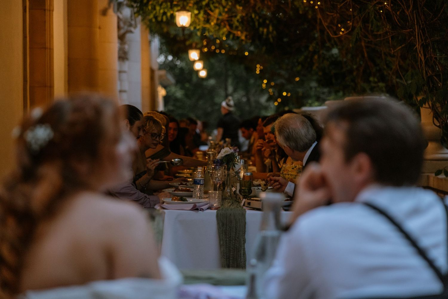 Wedding guests enjoy an elegant outdoor dinner reception with string lights and floral table settings.