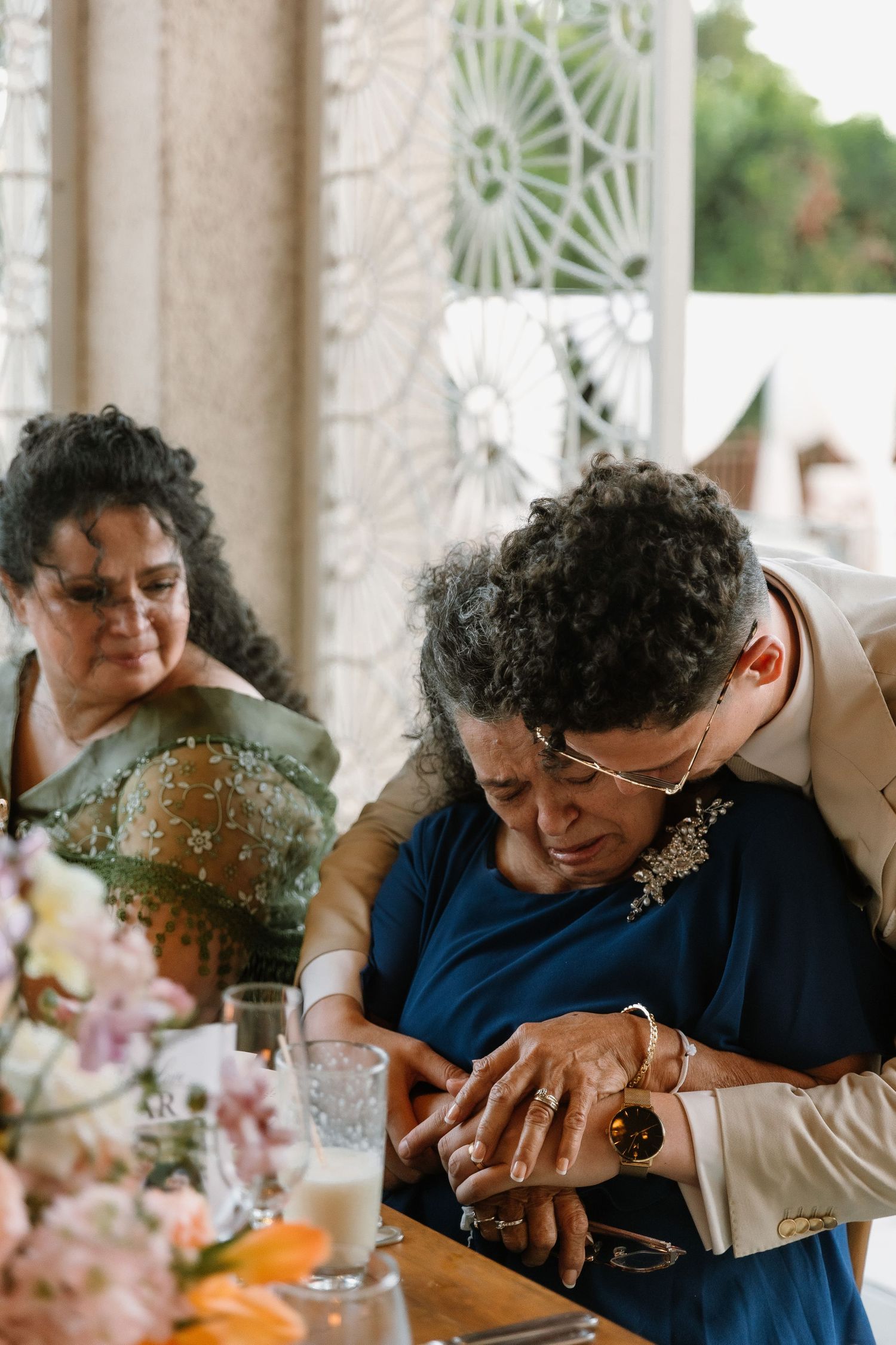 Elderly women sharing an emotional moment at a wedding reception table with floral centerpieces.