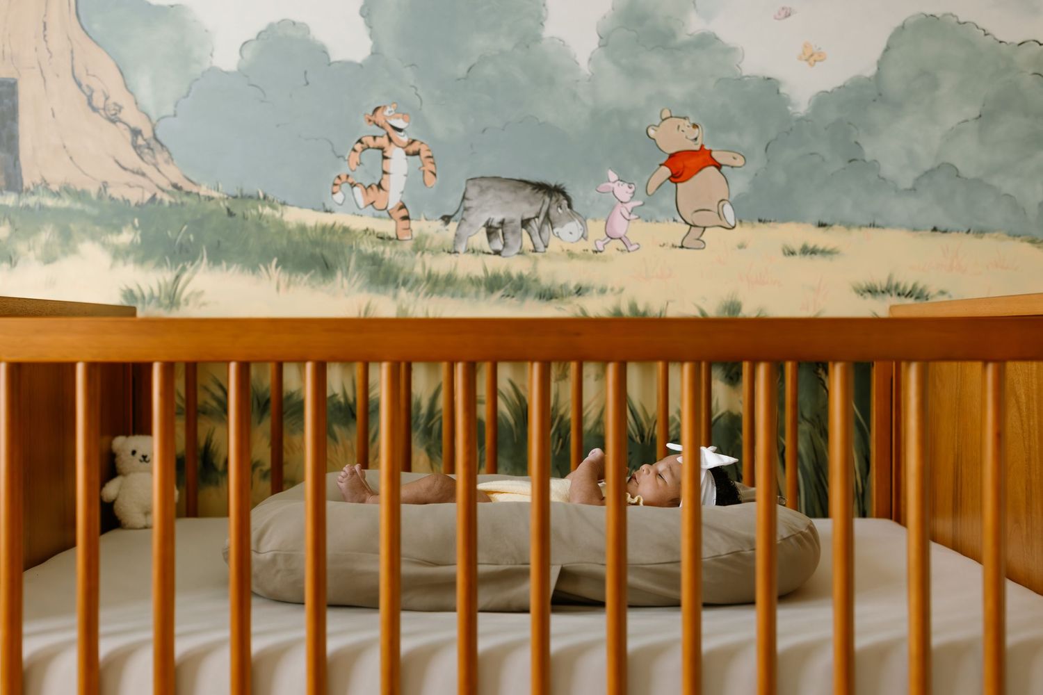 Wooden baby crib with Winnie the Pooh character mural painted on nursery wall featuring Tigger, Eeyore, and Pooh.