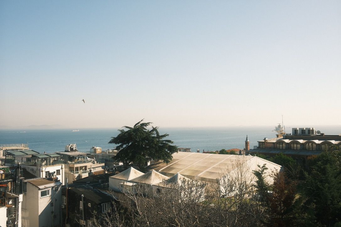 Aerial view of coastal city with white buildings, lush trees, and calm blue sea under a clear sky.