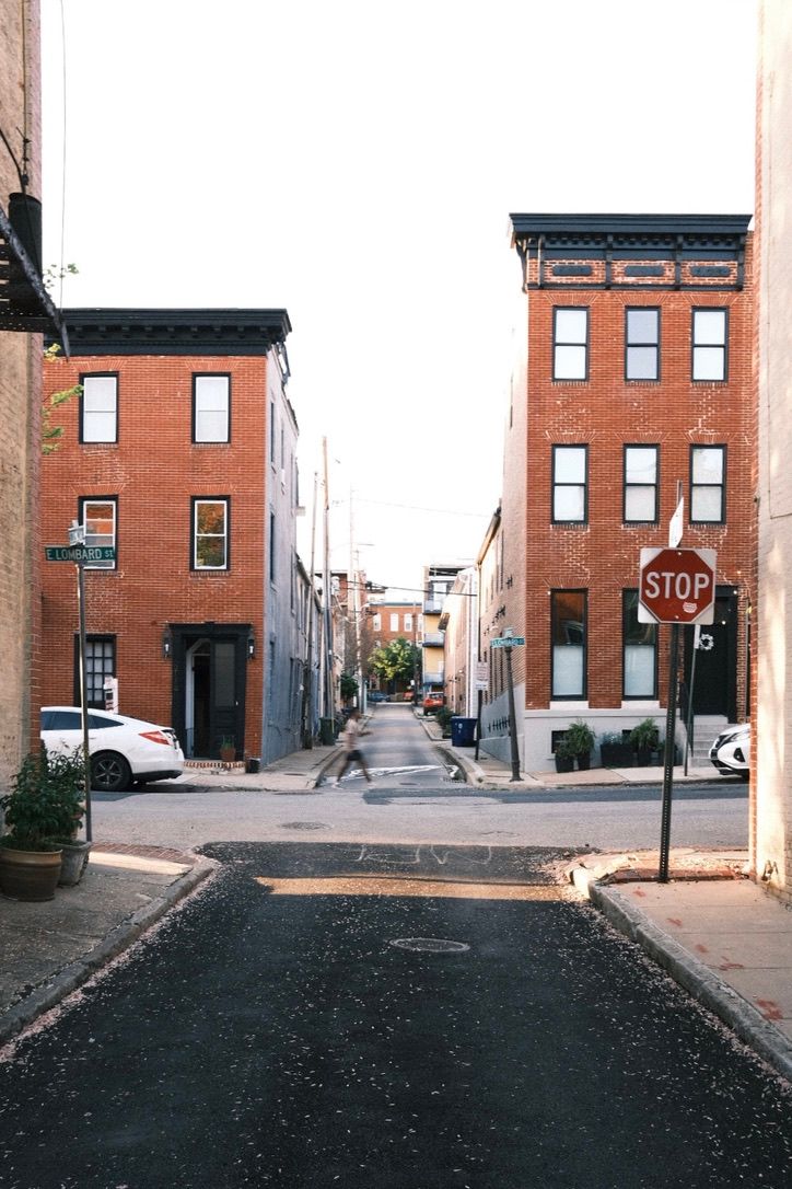 Red brick rowhouses line a narrow urban street with a stop sign in a classic American city neighborhood.