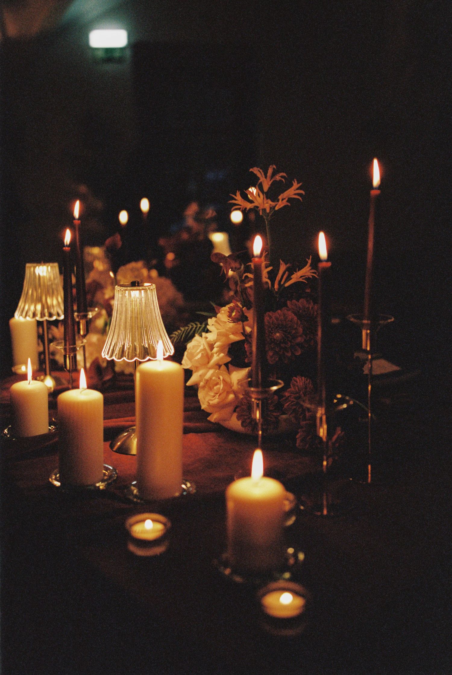 Romantic candlelit table with white pillar candles, taper candles, and fresh flowers creating an elegant ambiance.