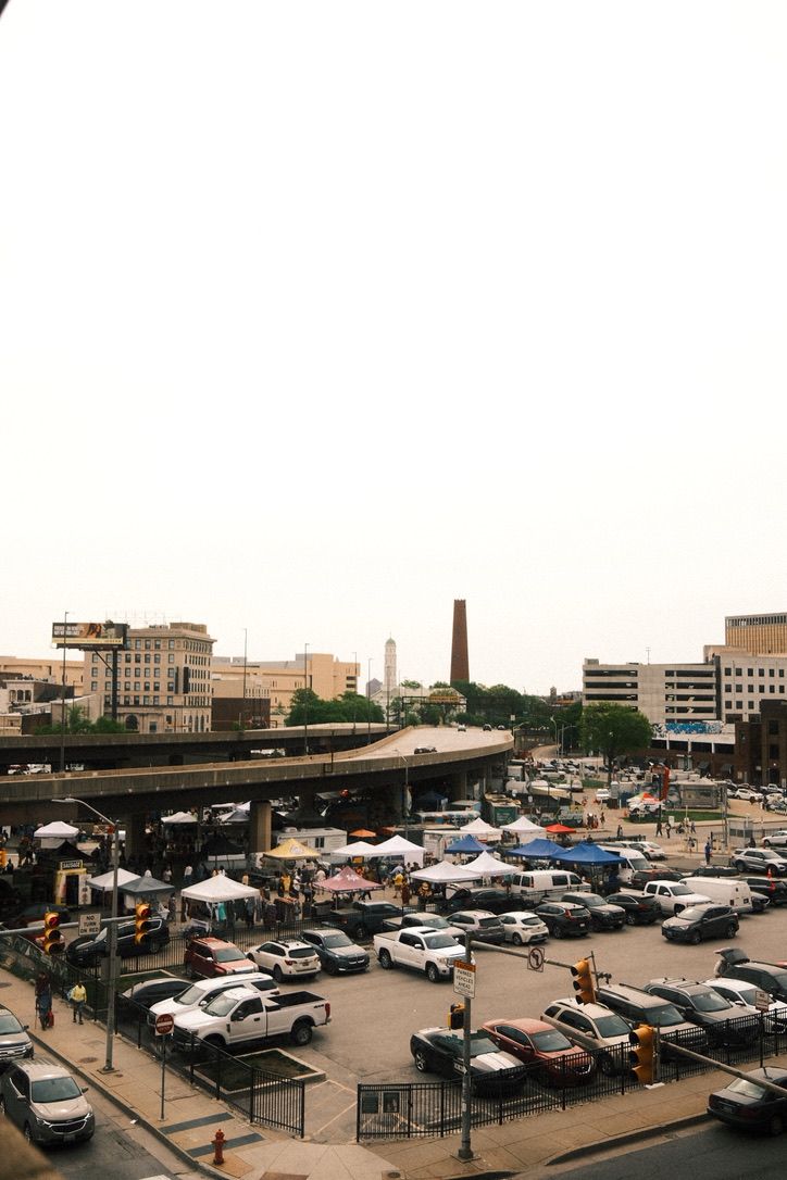 Aerial view of a busy urban outdoor market with white tents and parked cars near a highway overpass in a city.