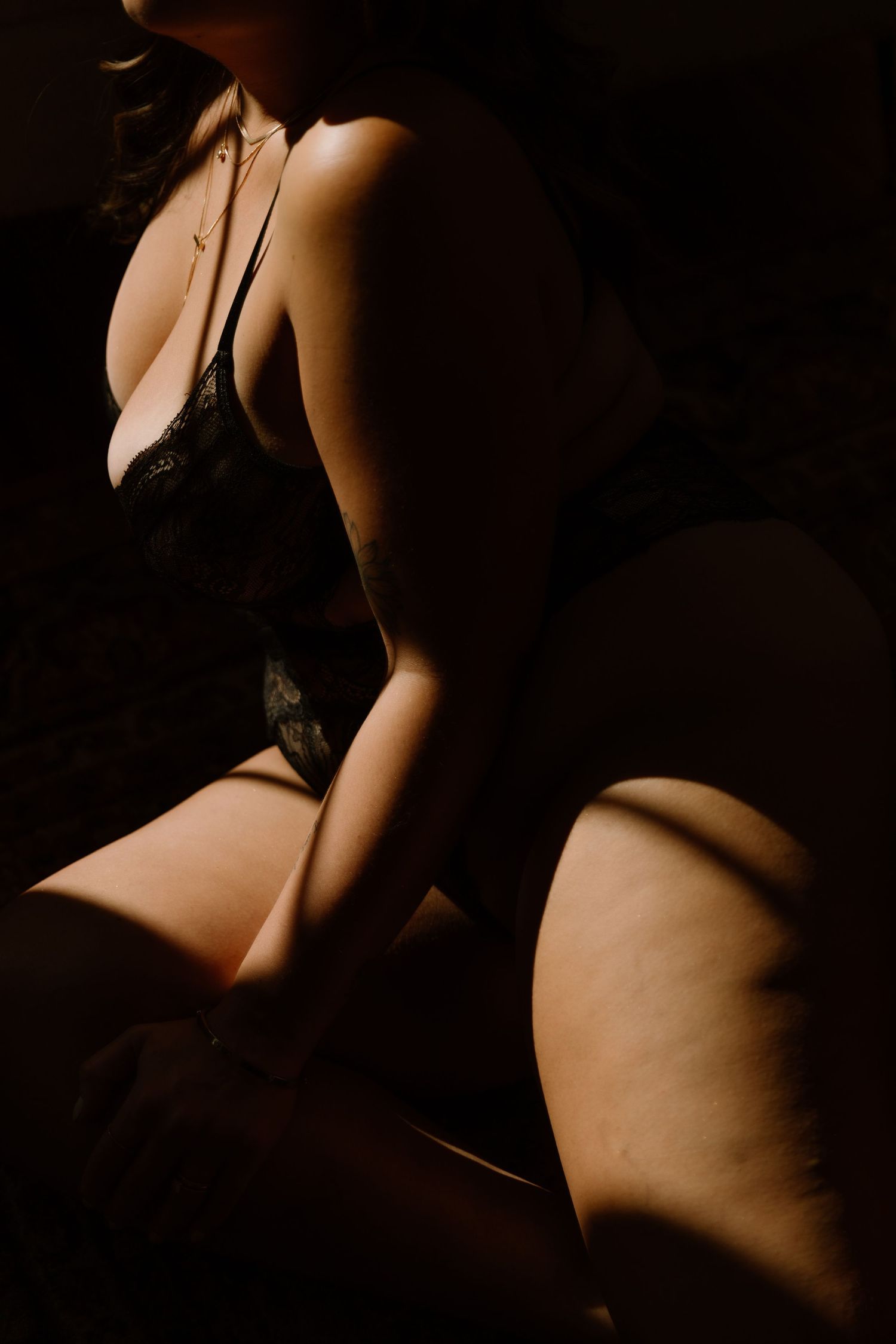 A woman in black lace lingerie poses in dramatic low-key lighting, highlighting curves and shadows.