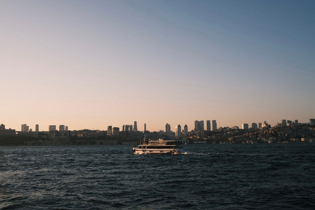 A ferry boat crosses the Bosphorus strait at dusk with Istanbul skyline in the background.