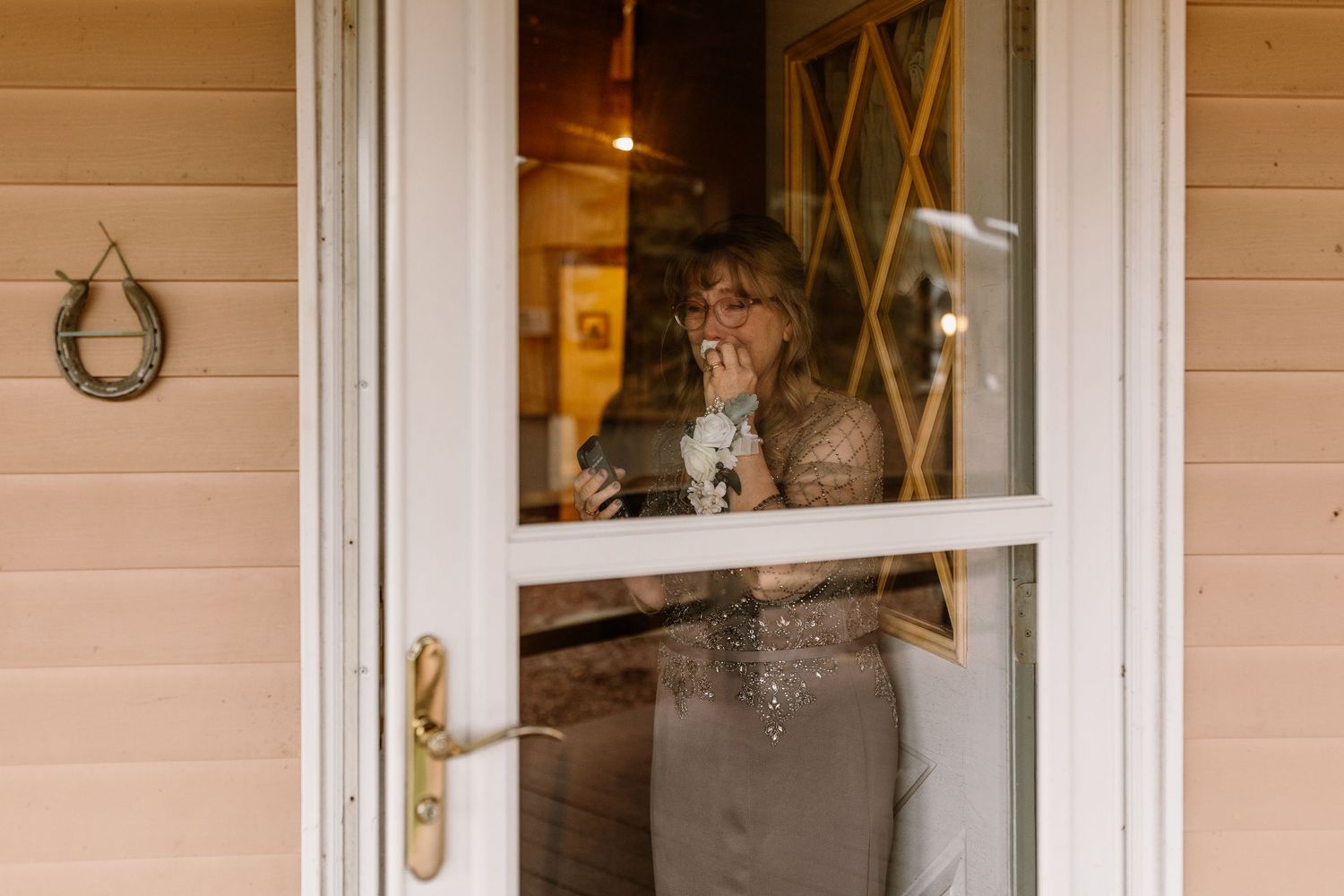 Tattooed woman smoking and holding a cup behind a glass storm door of a pink house.