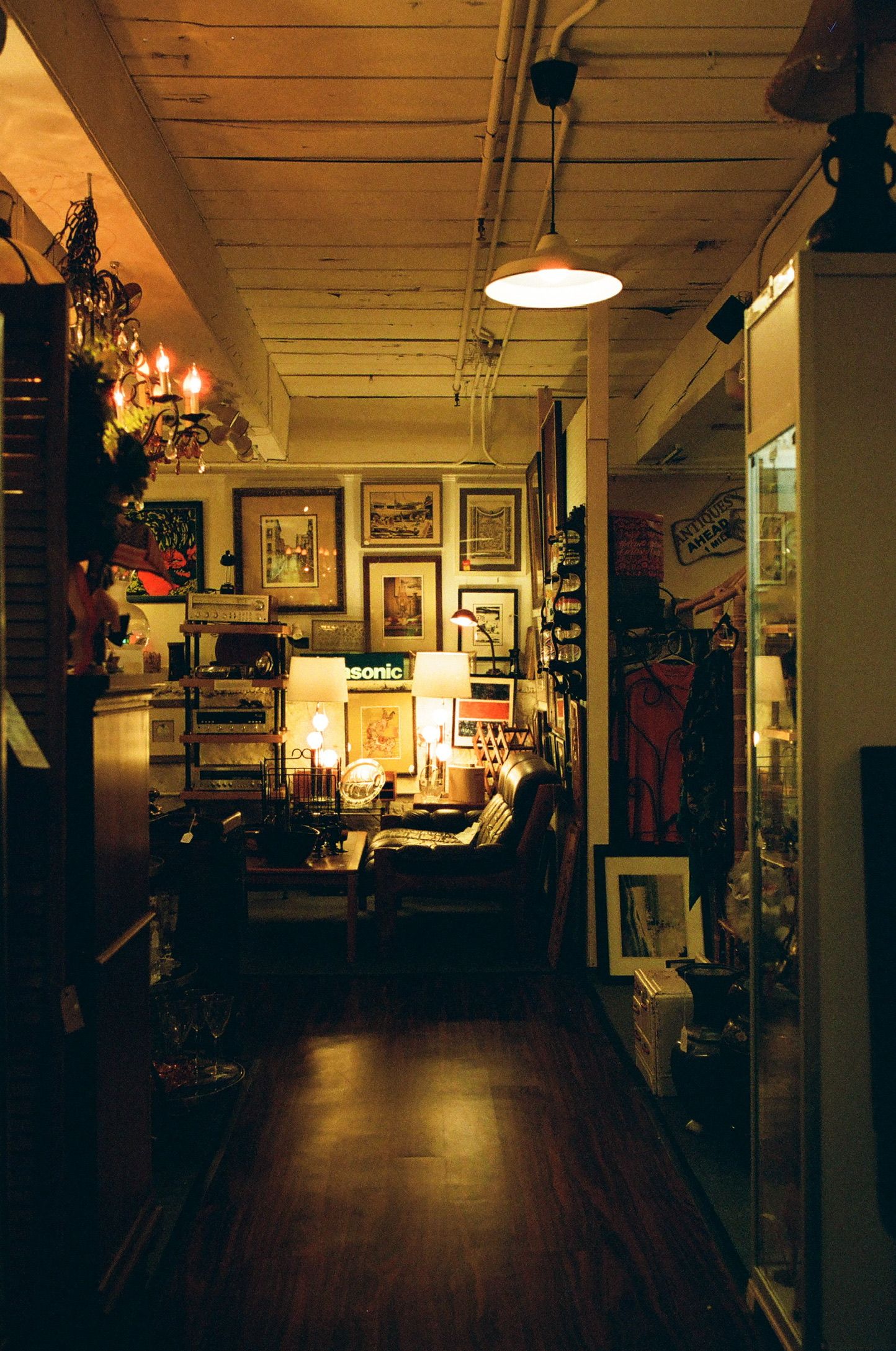Cozy antique shop corridor with warm lighting, framed artwork on walls, vintage furniture, and wooden floors.