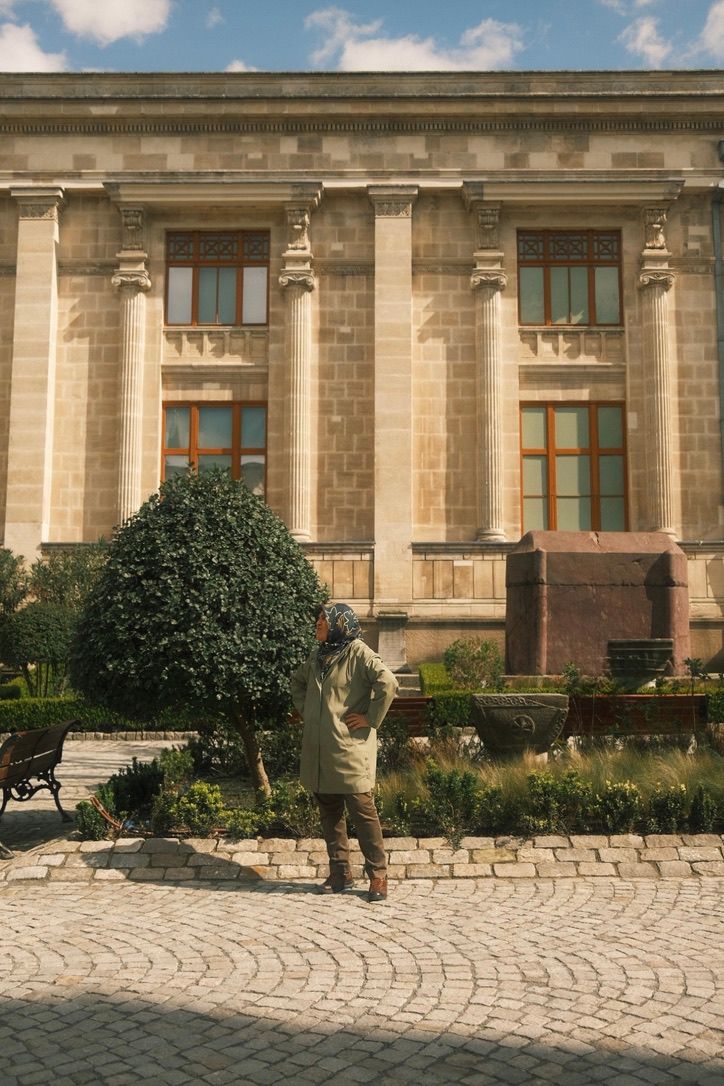 Person standing before a grand neoclassical building with tall columns in a cobblestone plaza.