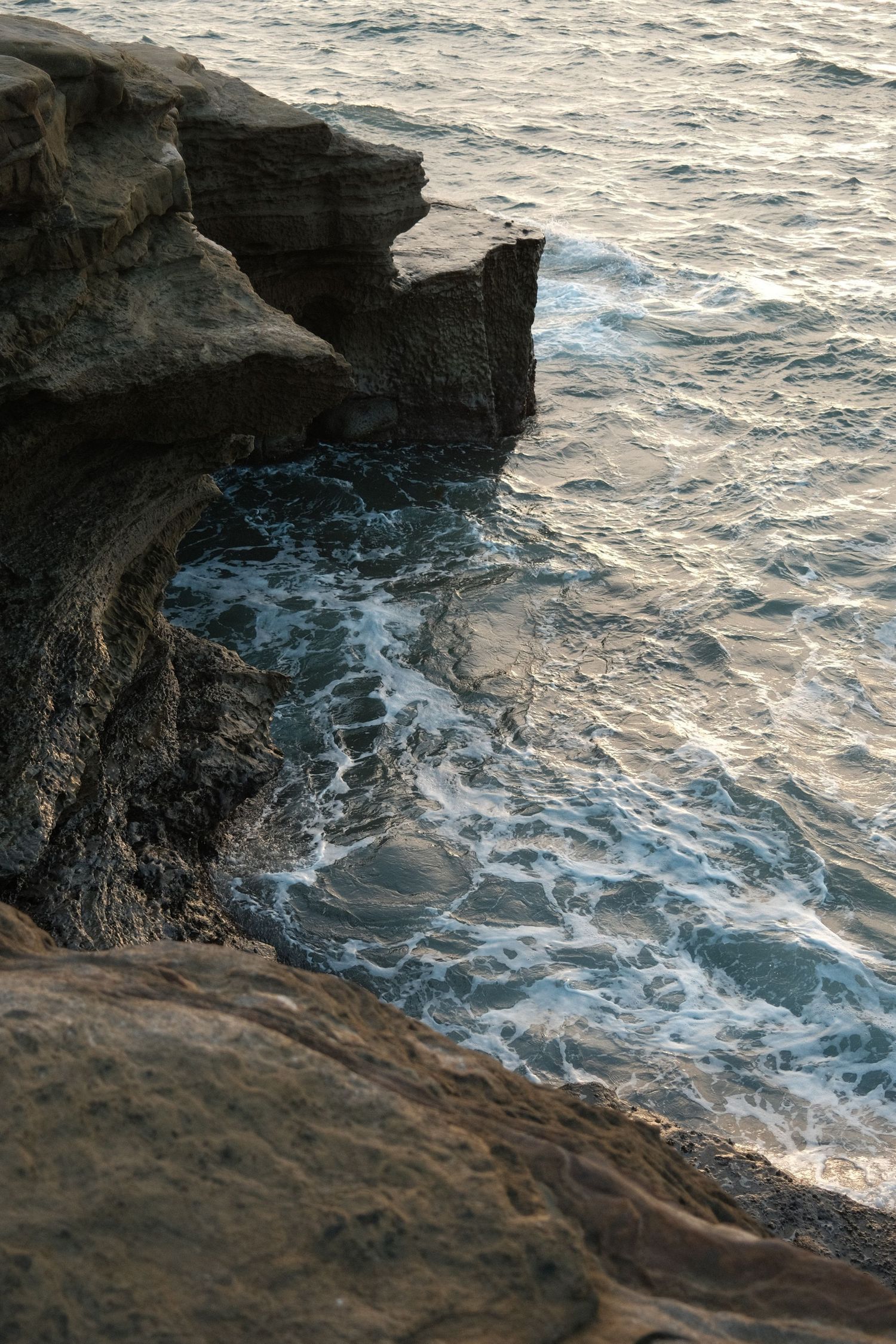 Rocky coastal cliffs with crashing ocean waves below, bathed in warm golden light at sunset.