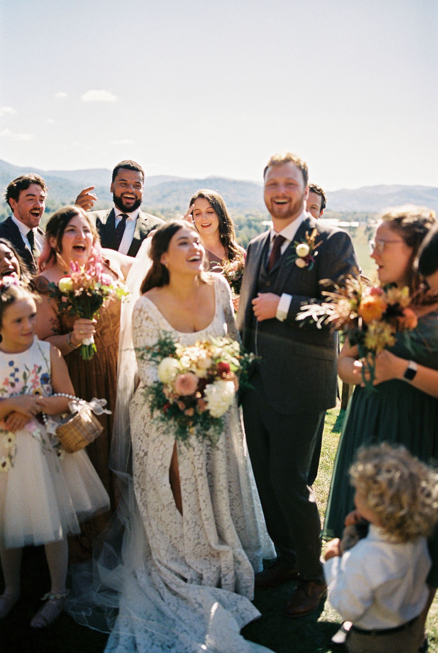 Joyful bride and groom celebrating with wedding party outdoors with mountain views.
