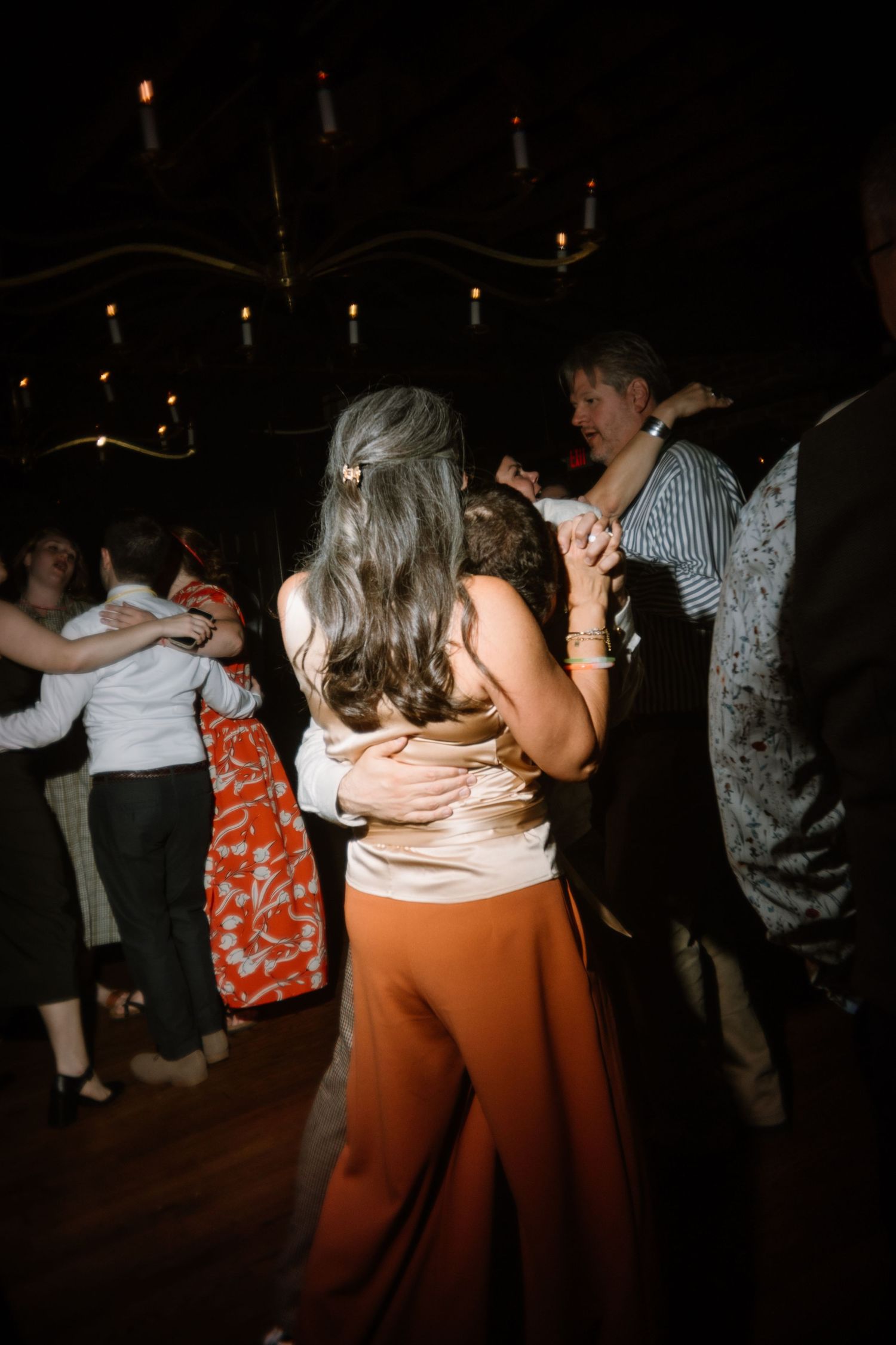 Couples dancing together in a dimly lit ballroom with candlelight ambiance at a formal evening event.