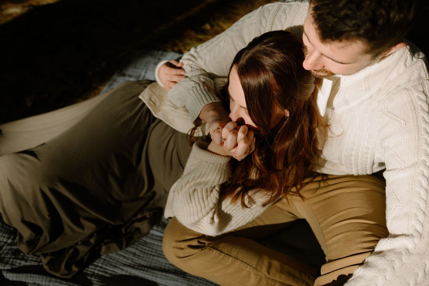 Couple sharing a tender moment, woman resting head on mans lap while sitting on a blanket outdoors.