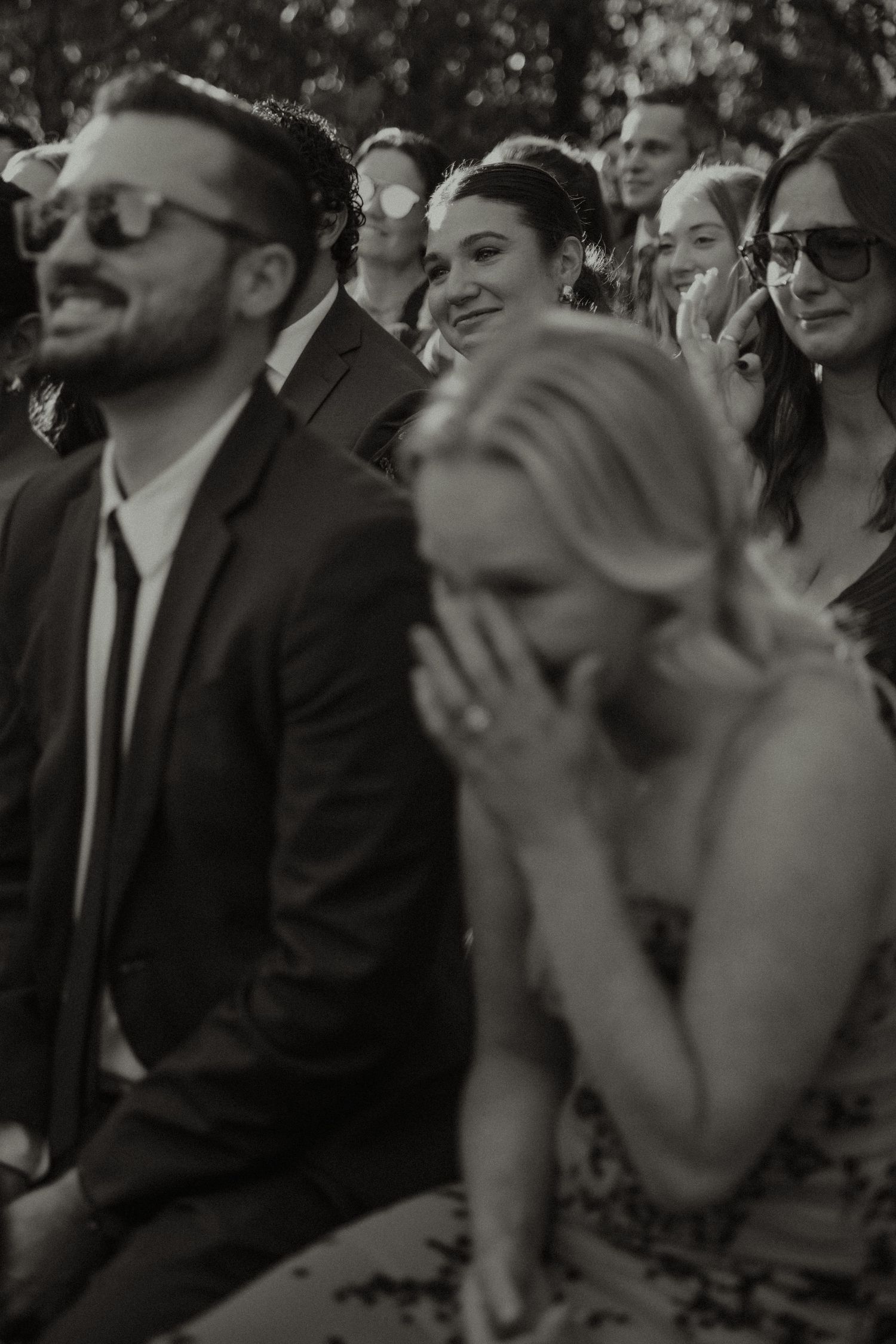 Black and white photo of emotional wedding guests laughing and crying during an outdoor ceremony.