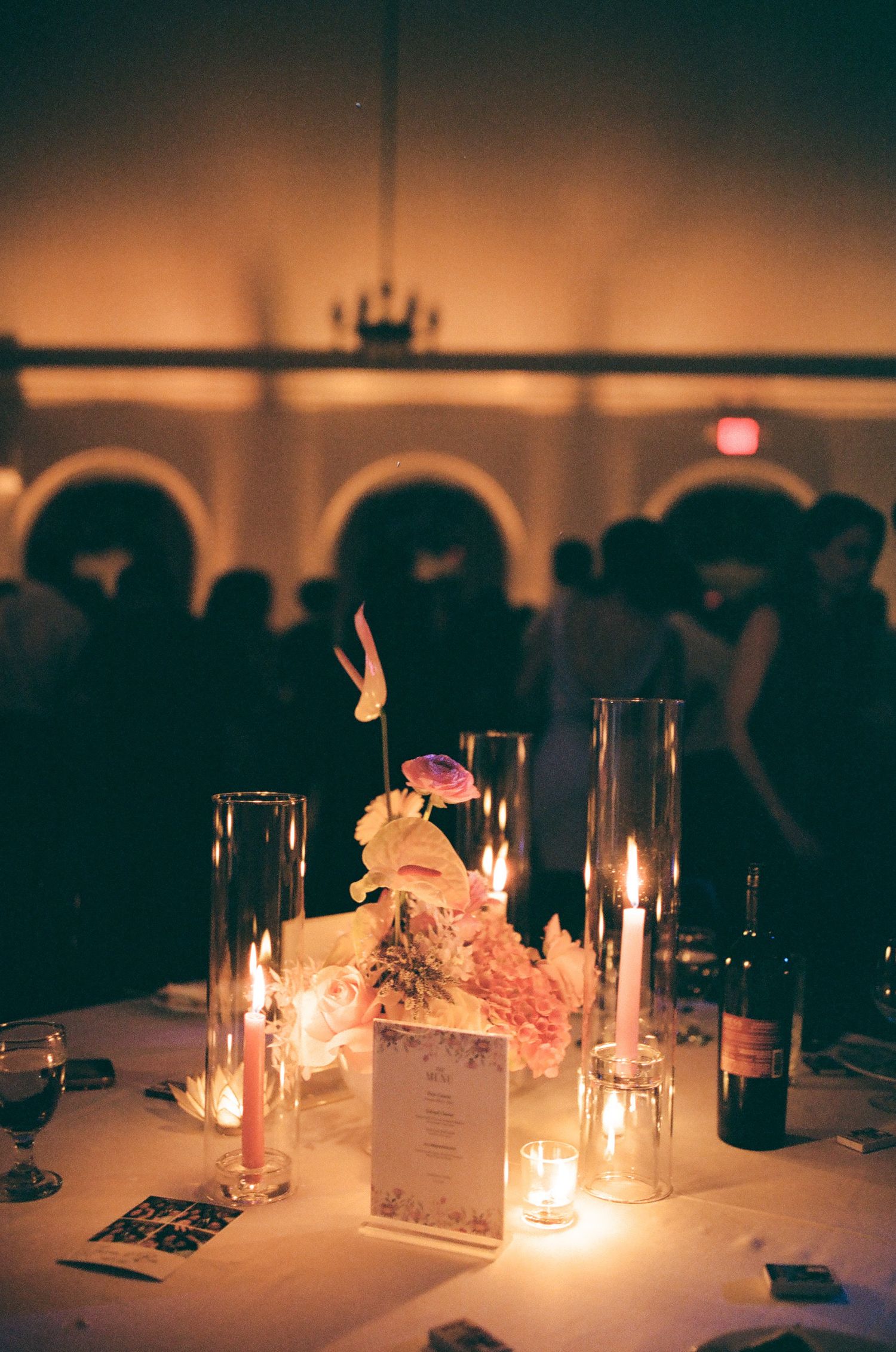 Romantic wedding reception table with candlelight, floral centerpiece, and wine bottle in dimly lit ballroom.