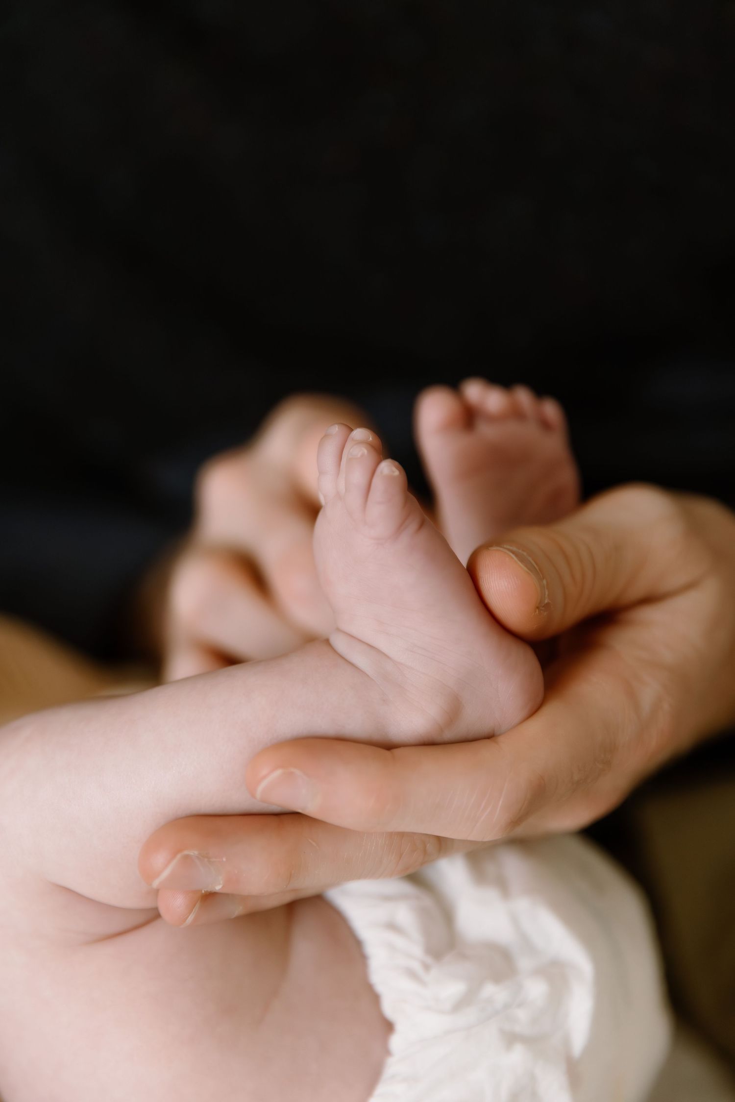 Adult hands gently cradling tiny newborn baby feet against a dark background.