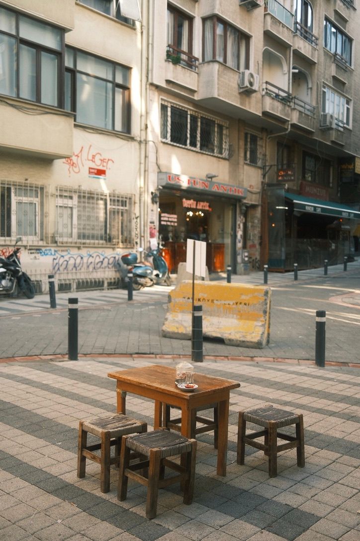 Wooden table and stools on a cobblestone street corner with urban buildings and shops in the background.
