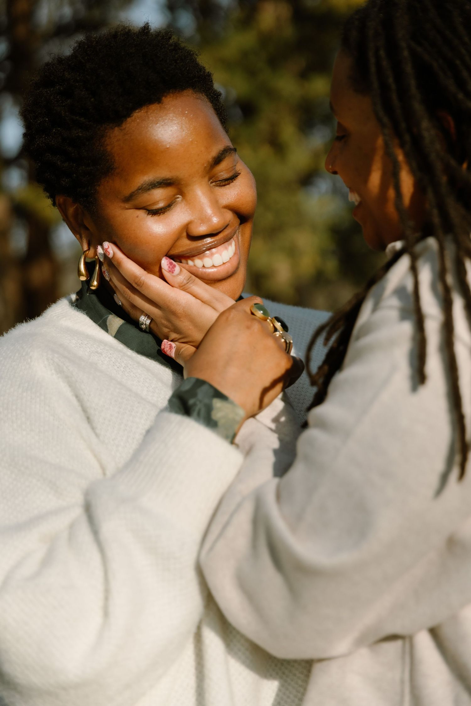 Two Black women sharing a joyful moment outdoors, one smiling as the other gently cups her face.