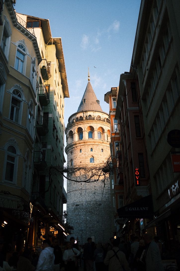 Historic Galata Tower rises above narrow Istanbul streets lined with shops and pedestrians at golden hour.