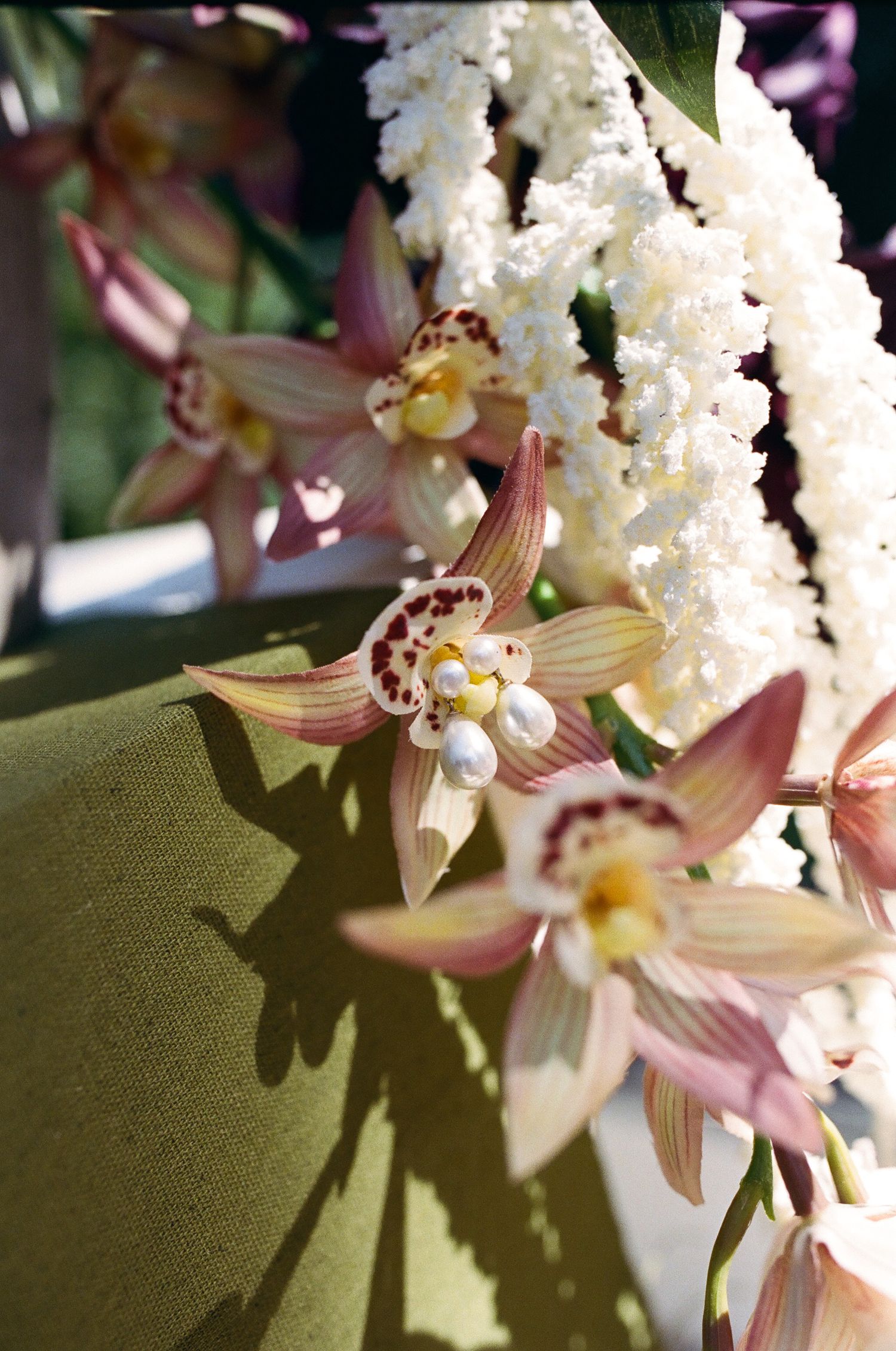 Pink and white cymbidium orchids with dark speckles arranged with fluffy white astilbe flowers against a green background.