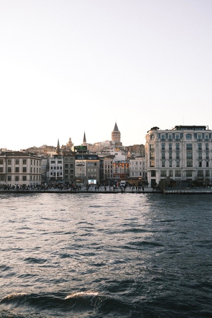 Waterfront view of Istanbul skyline with Galata Tower and historic buildings along the Bosphorus strait at sunset.