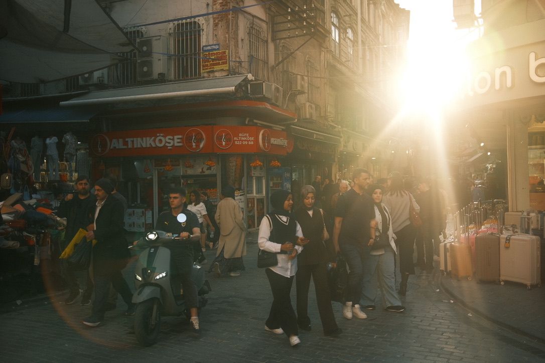 Busy street scene at golden hour near a kebab shop with pedestrians and a scooter in an urban setting.