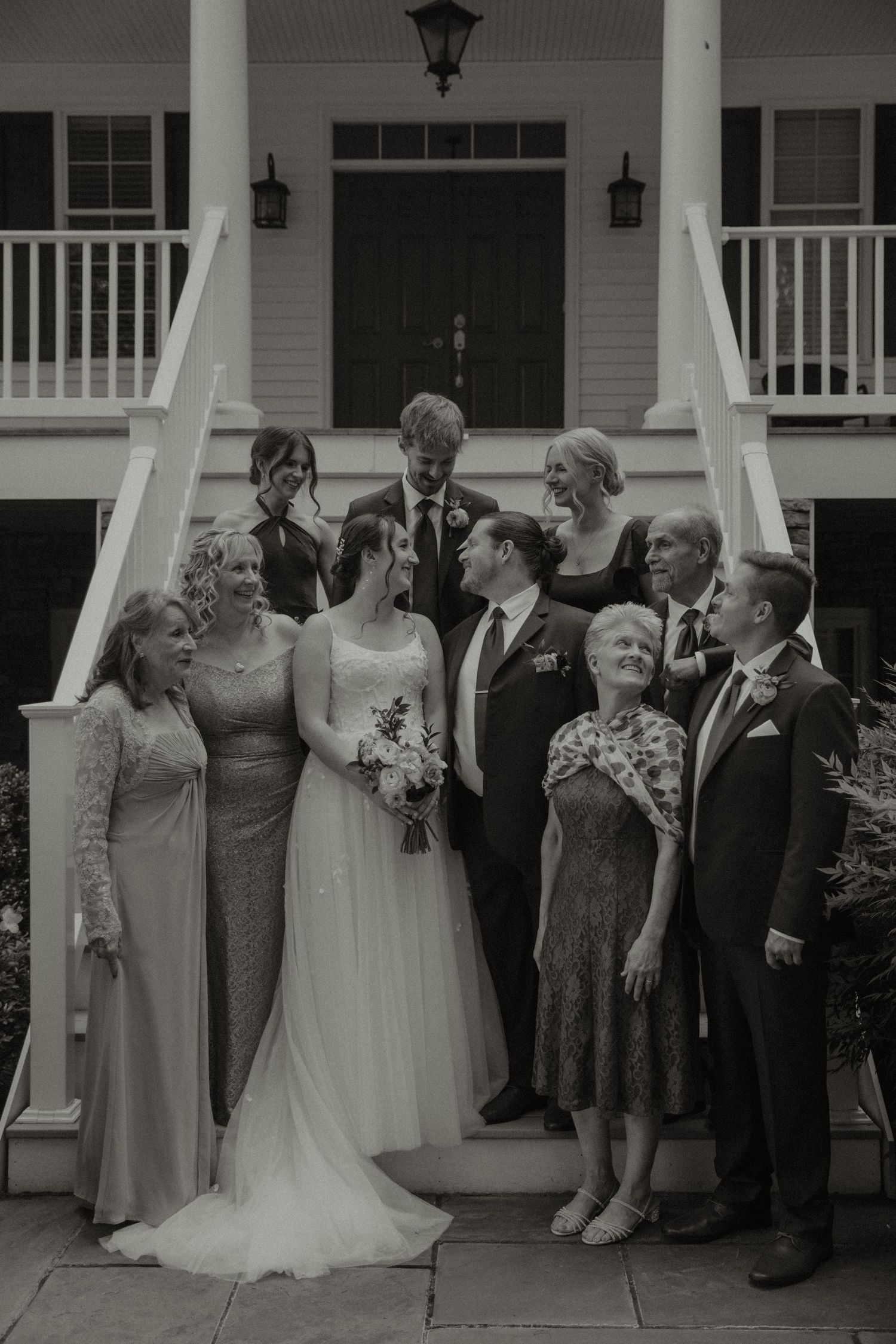 Black and white wedding photo of bride, groom, and family posing on steps of elegant venue.