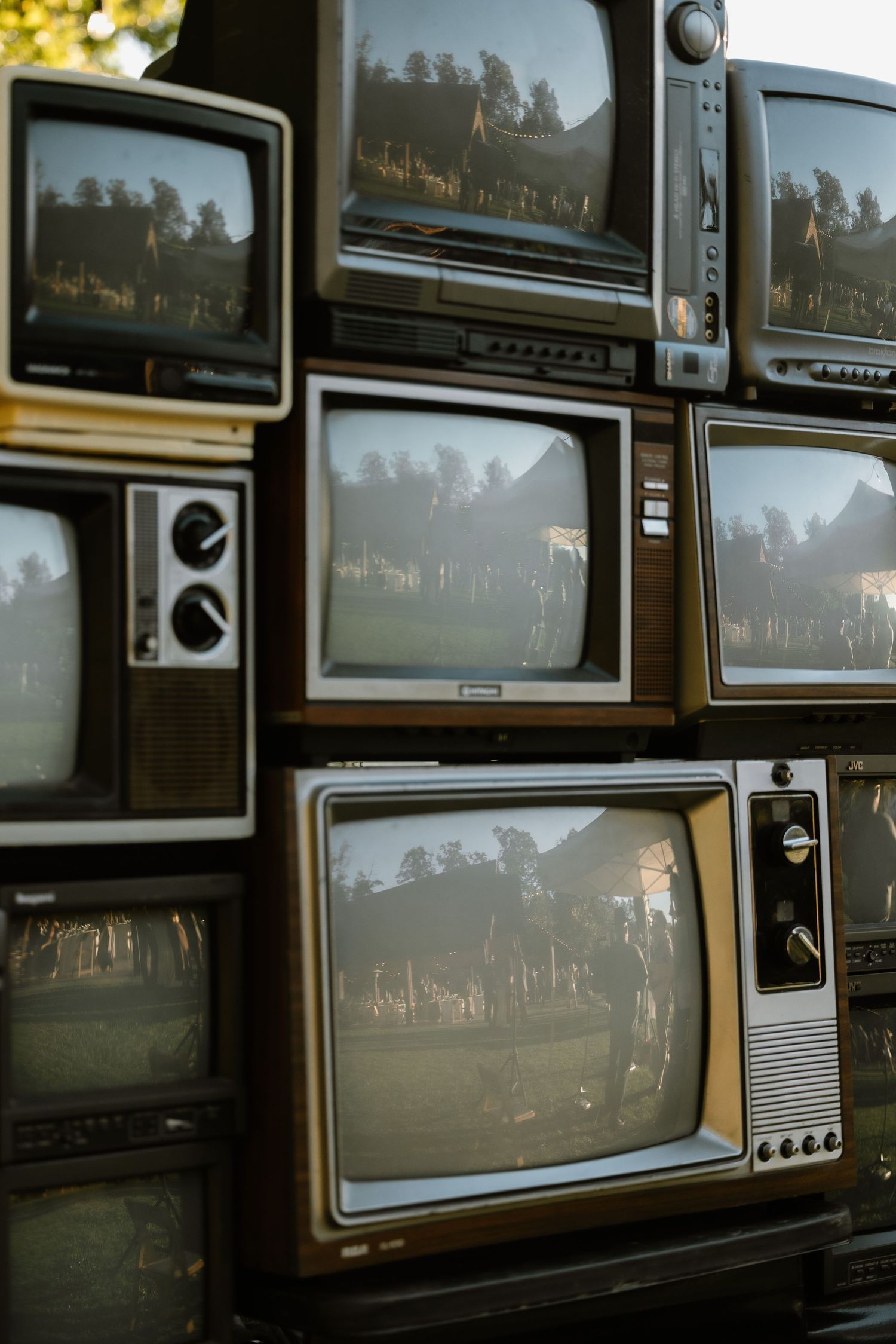 Stack of vintage retro CRT televisions displaying nature scenes, arranged in a wall formation outdoors.
