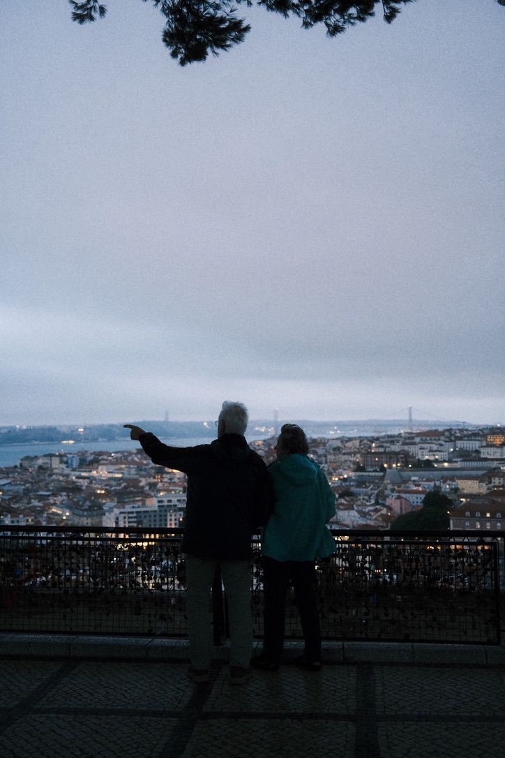 Couple silhouetted at dusk overlooking a city skyline and river from a scenic viewpoint with a bridge in the distance.