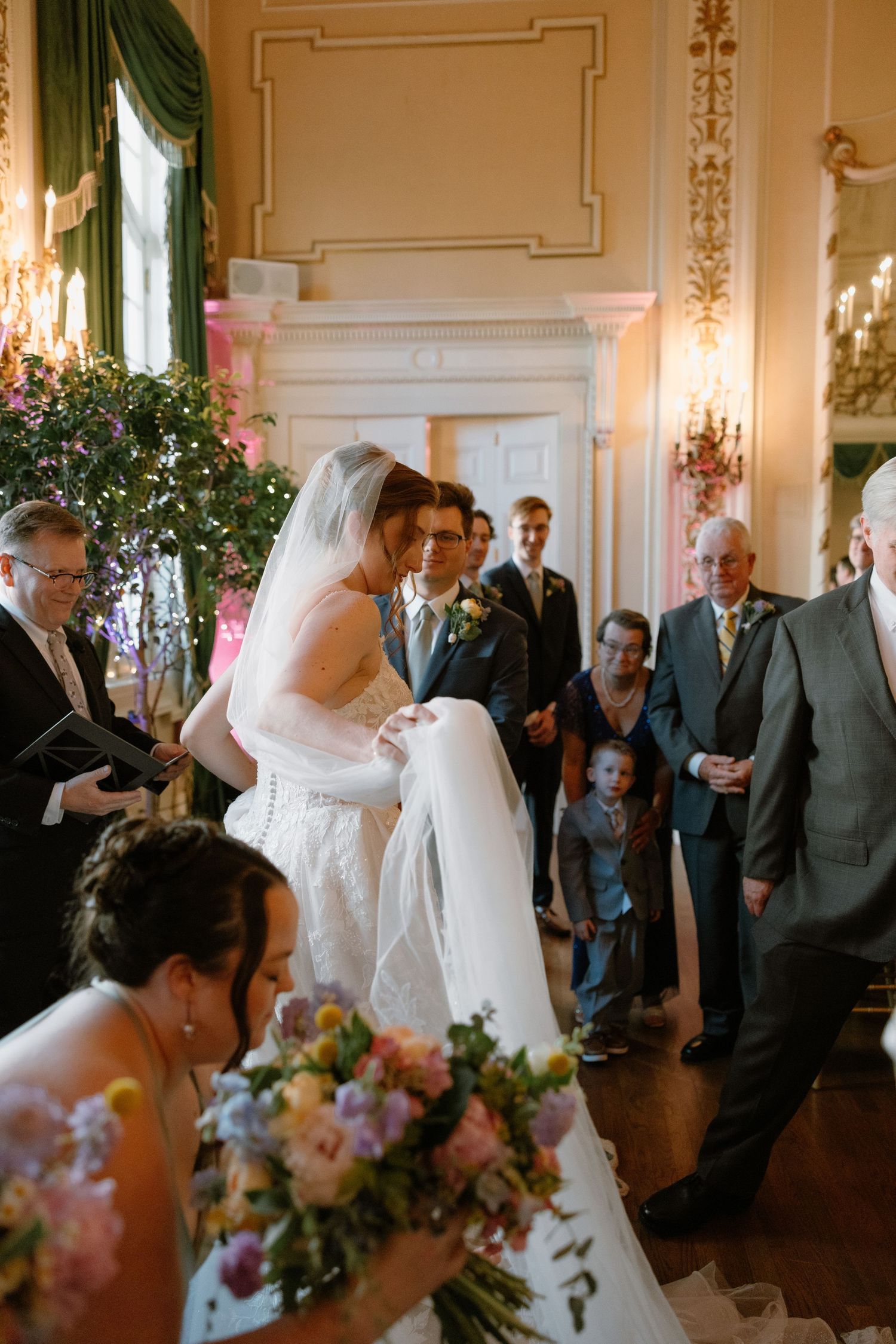 Bride and groom share a tender moment at the altar during an elegant indoor wedding ceremony with guests looking on.