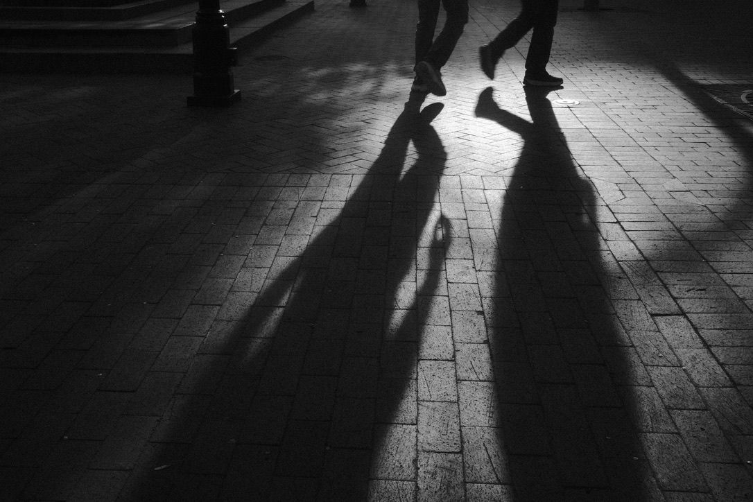 Black and white photo of two people walking, casting long dramatic shadows on a tiled pavement.