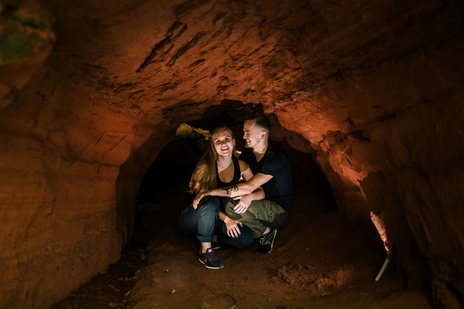 Couple sitting in a red sand stone cave and holding each other, smiling, dramatic and mysterious lighting