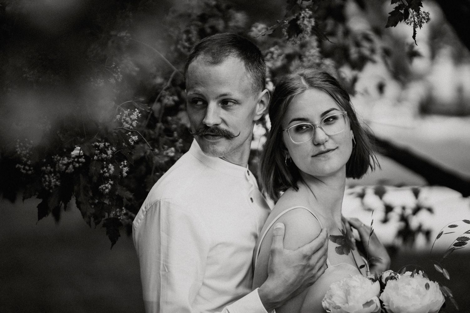 Cinematic black and white photo of a groom and bride, husband holding her shoulders, both dramatically looking on the side