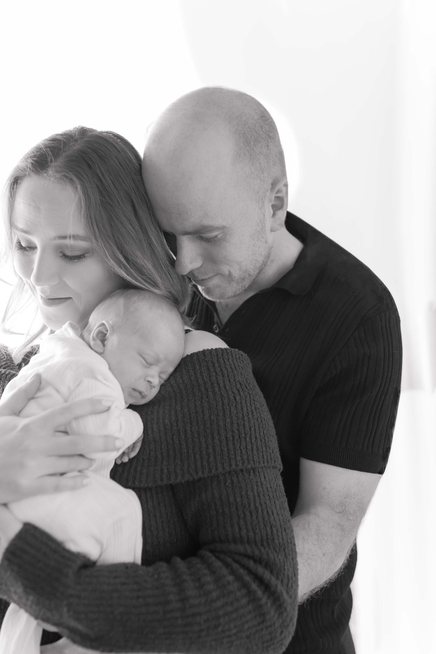 Mum holding newborn boy with dad hugging mum from behind