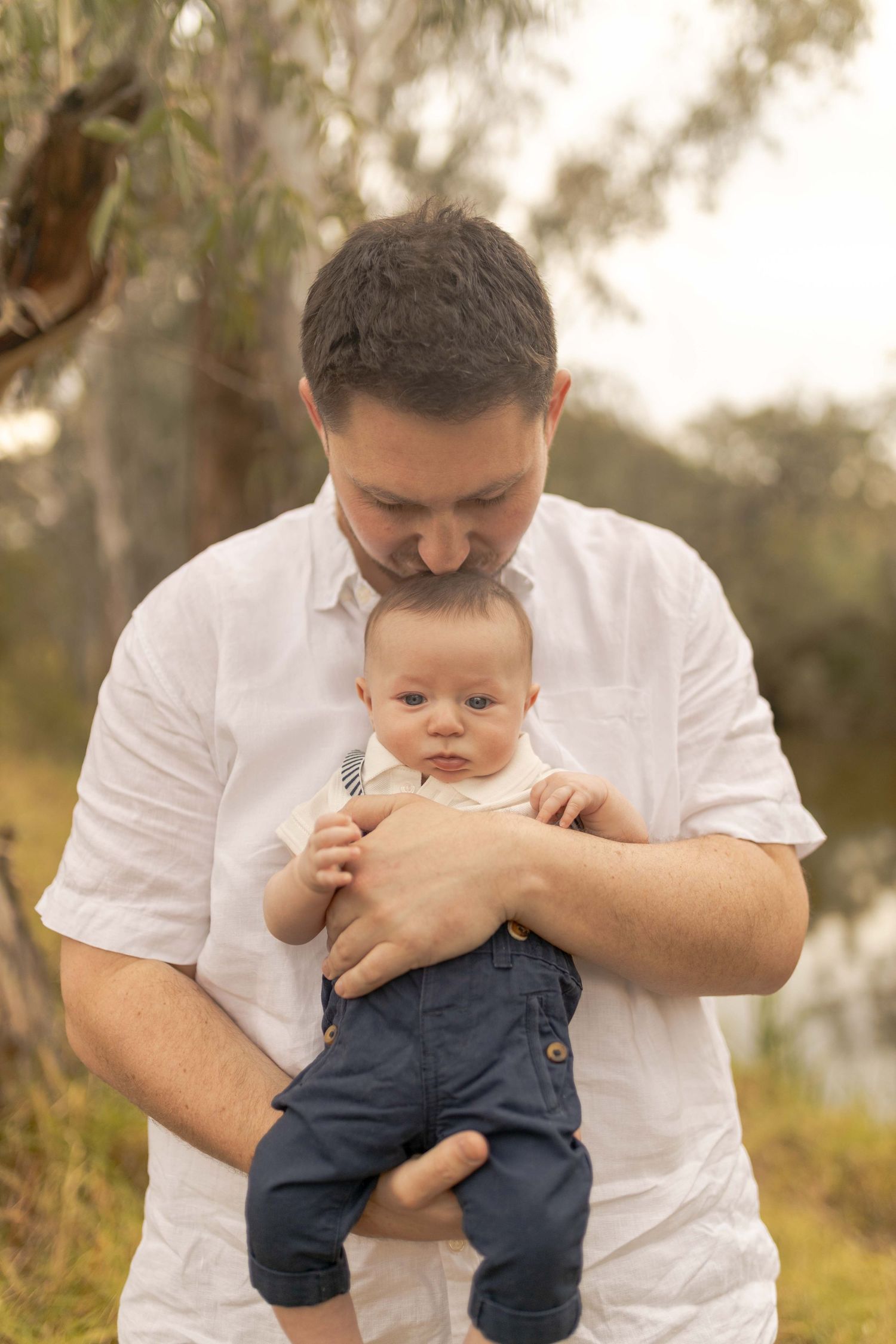 Dad holding baby in front of him and kissing baby on the head Outdoor family session Sunshine North Melb Vic