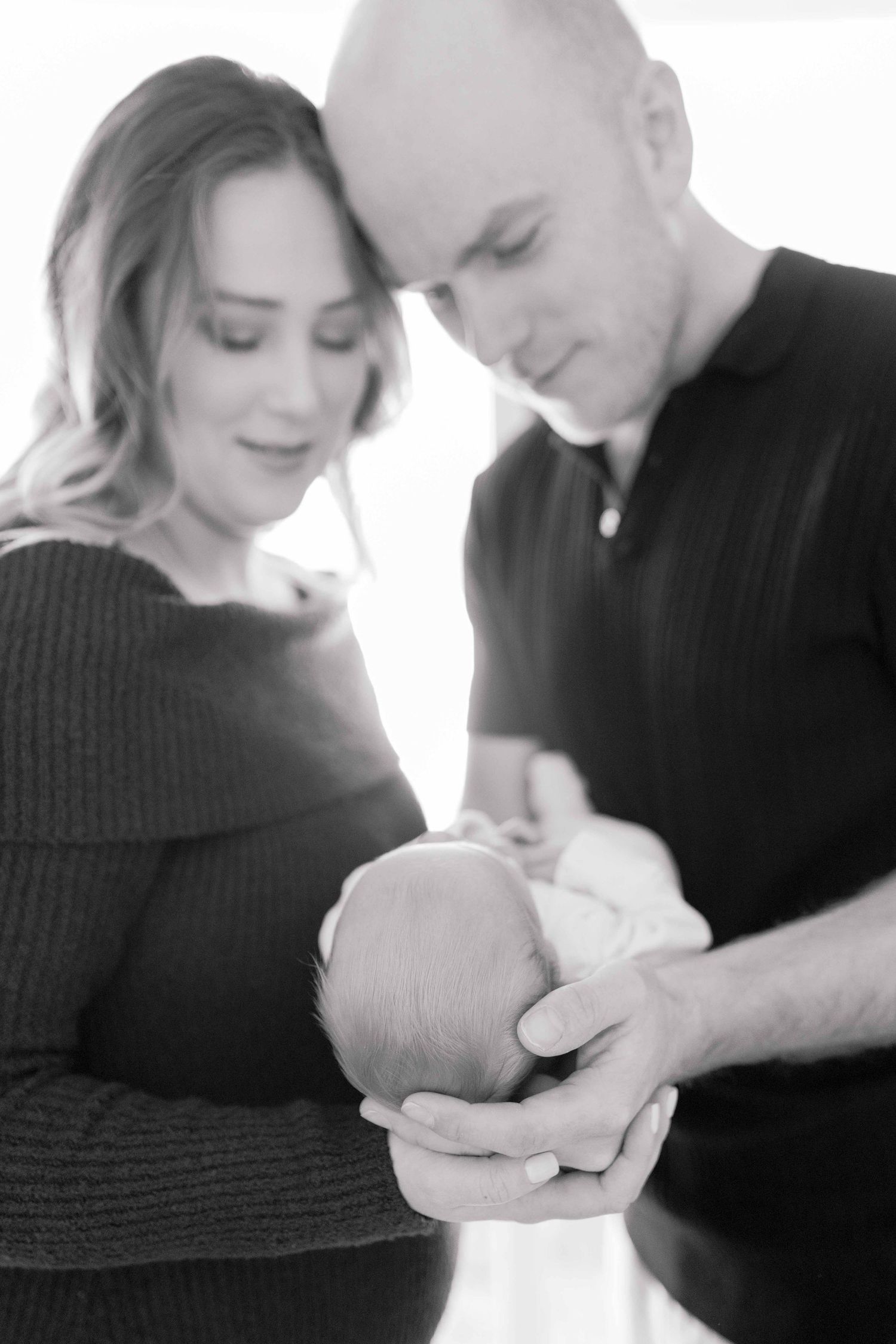 Parents smiling at each other holding their newborn between their hands
