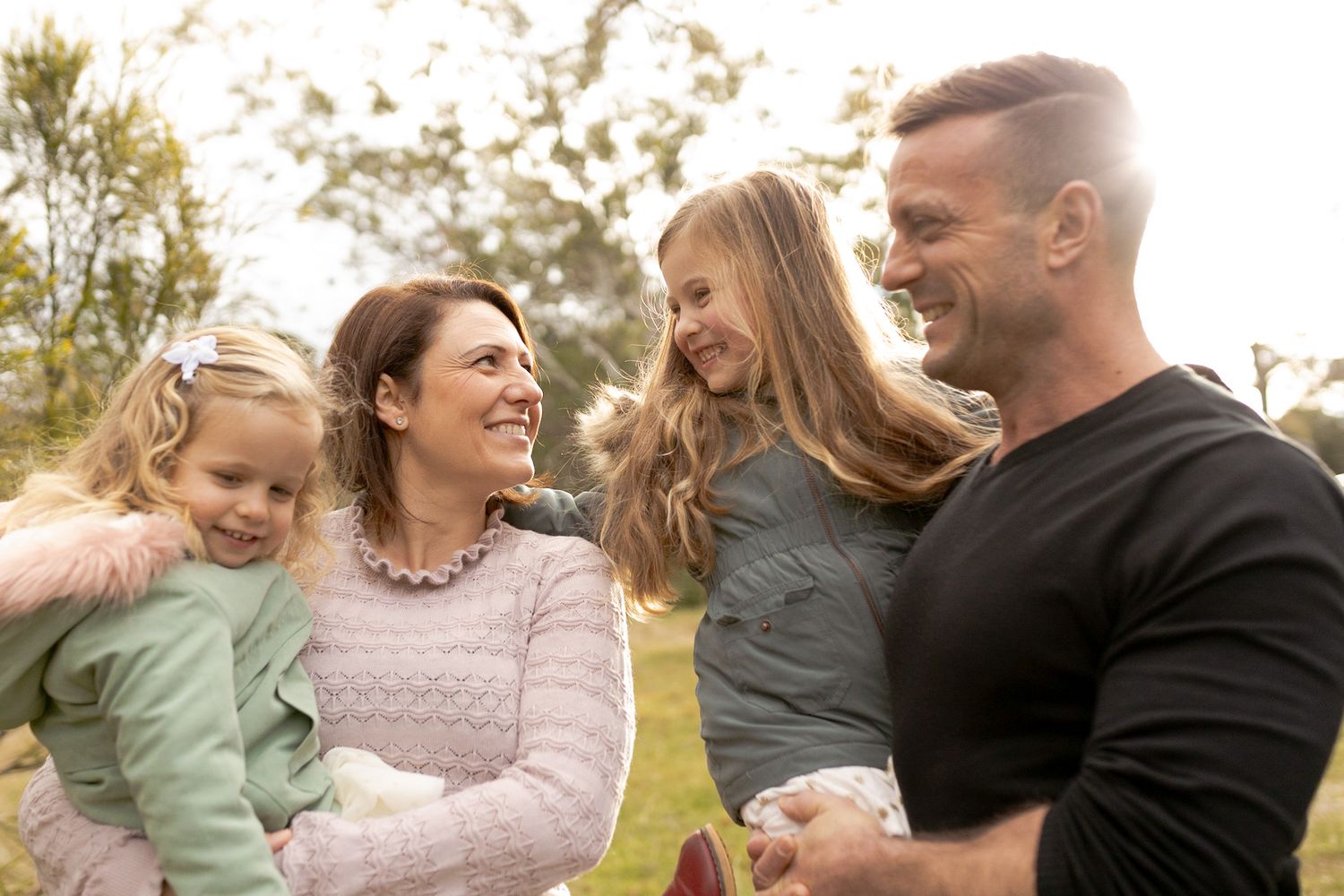 Family of four holding each other happily looking at each other 2 girls outdoor family session Macedon Ranges, Melbourne, Victoria