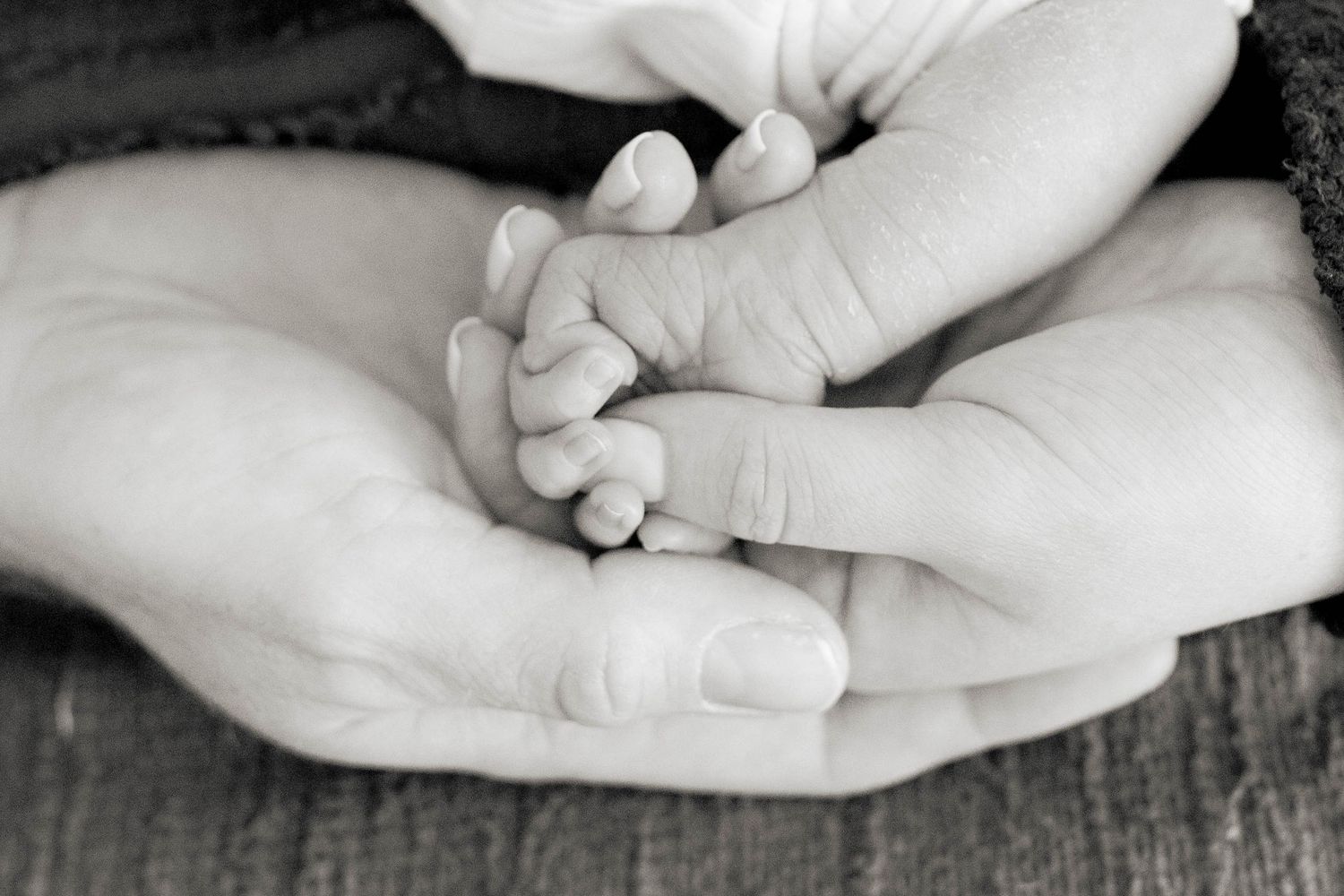 Mum, dad and newborn lying hands on top of each other