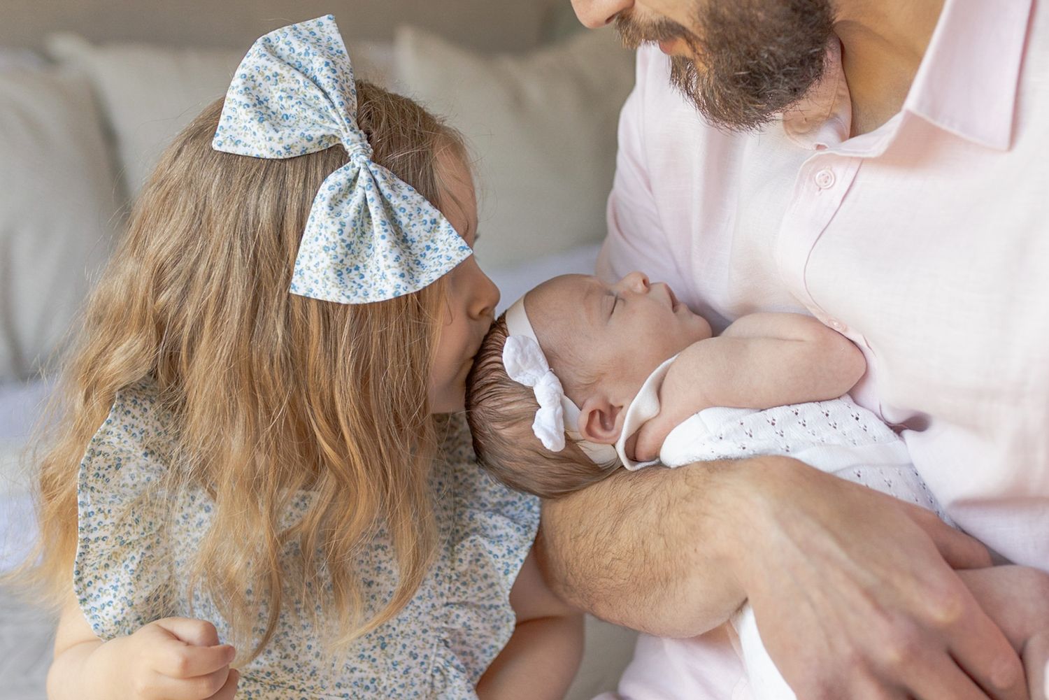 Dad holding newborn girl and big sister kissing little sister on the head at home newborn session Caroline Springs Melb Victoria
