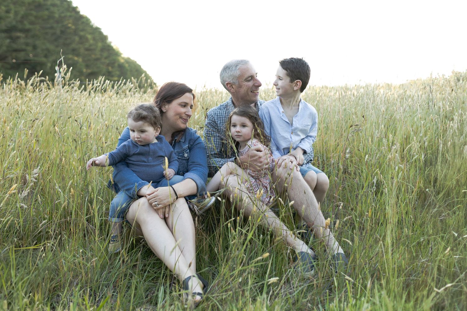 Family of five holding each other happily looking at each other. in a field with tall grass Outdoor at home fam Woodend, Melbourne, Victoria