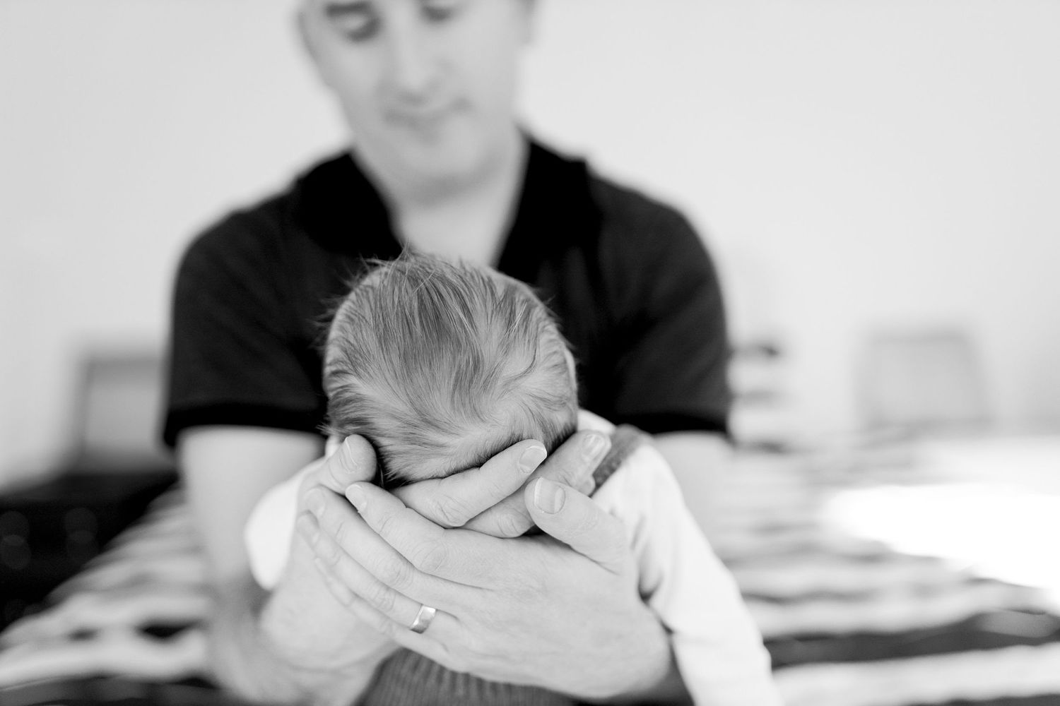 Dad holding newborn baby boy in his hands while sitting on the bed at home newborn session  Moonee Ponds Melb