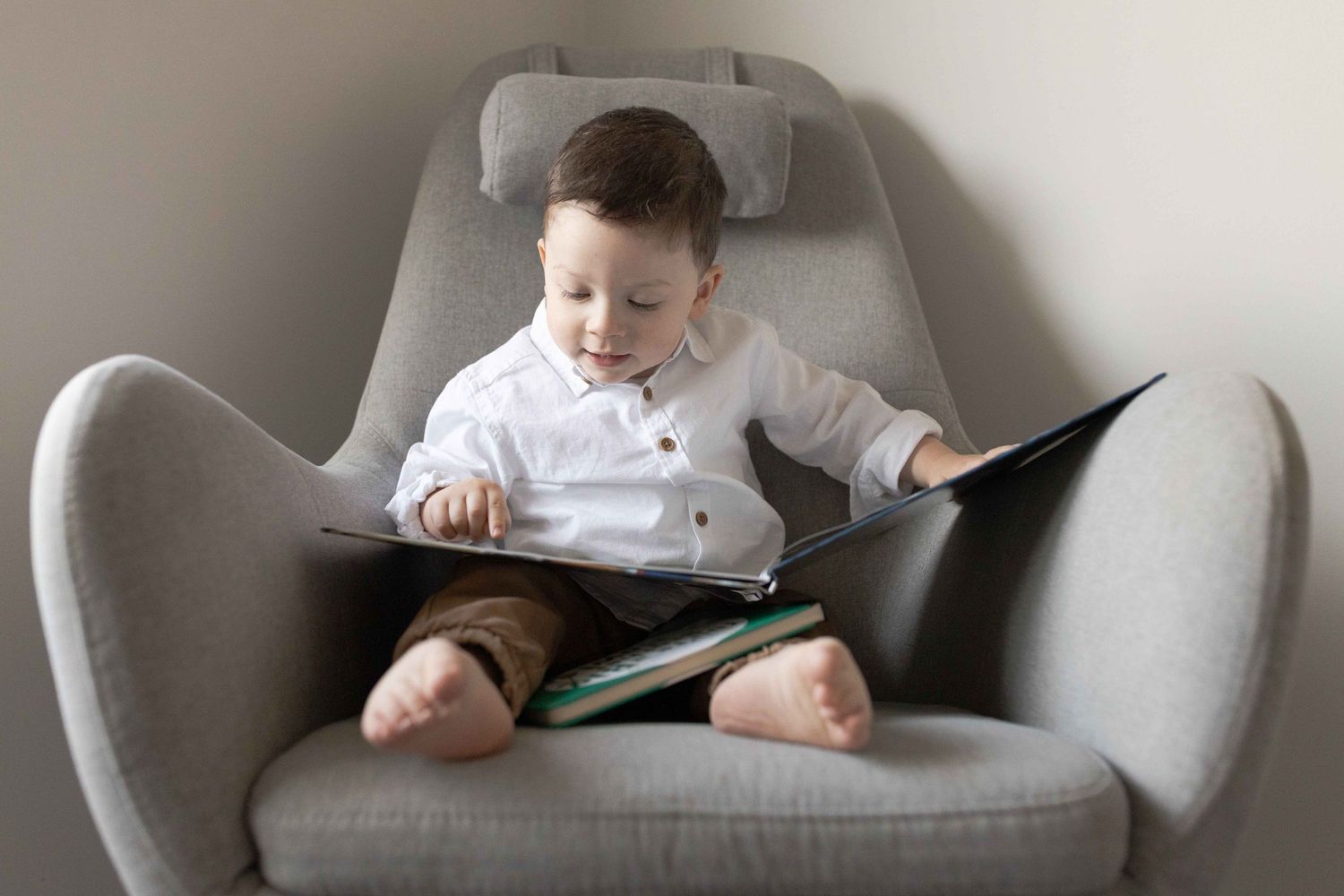 Toddler sitting in a big chair and reading a book at home newborn session  Tullamarine Melb Vic