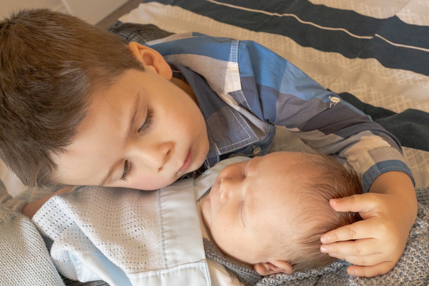 Brothers lying on the bed snuggled together while lying on the bed baby swaddled in blue blanket at home newborn session  Moonee Ponds Melb