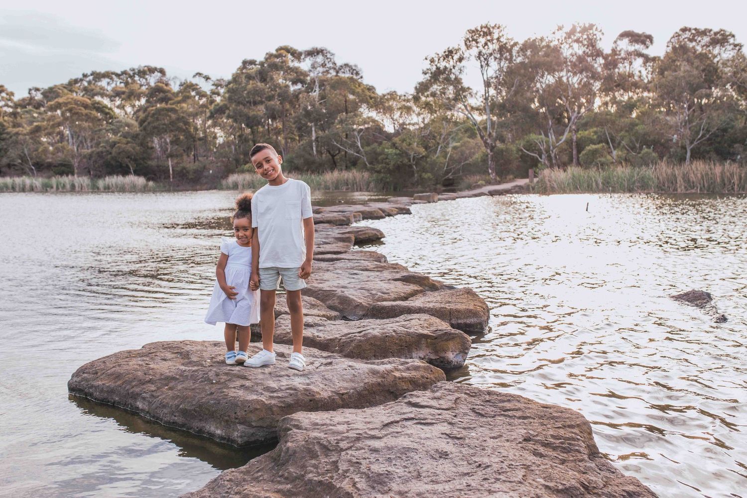Brother and sister holding hands standing on the rocks across a lake Newport Lakes, Melbourne, Victoria