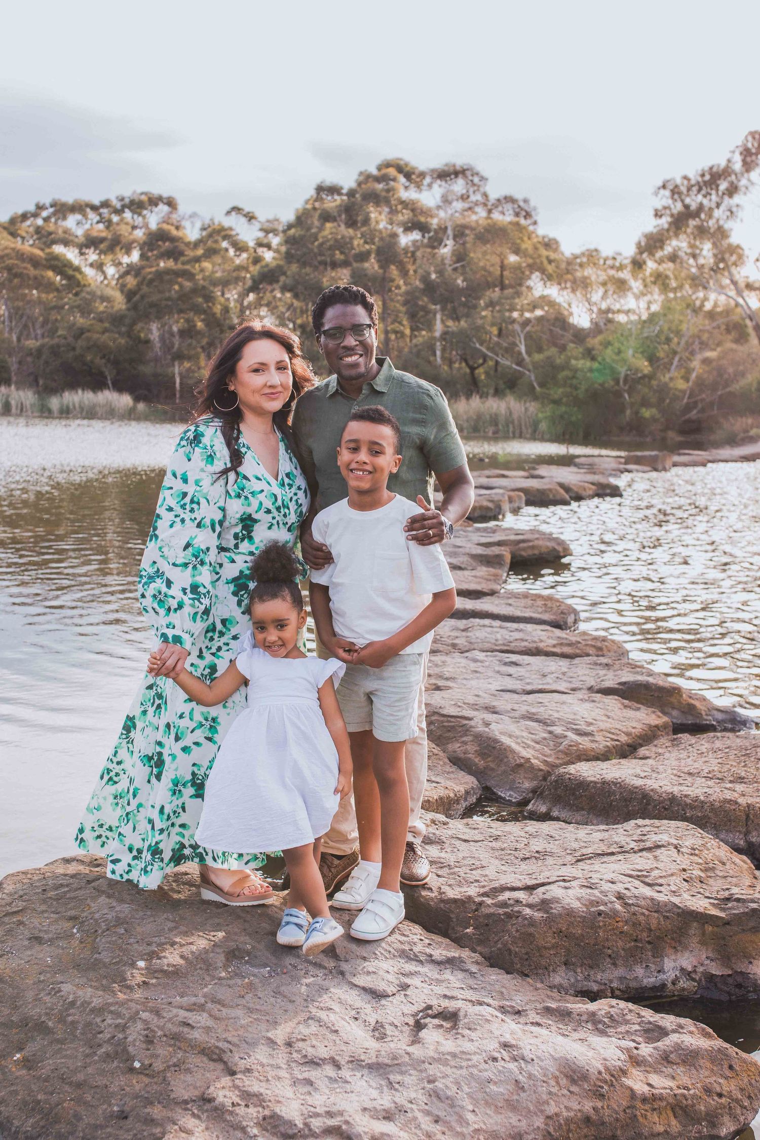 Family of four holding each other happily standing on the large rocks, looking at each other. Newport Lakes, Melbourne, Victoria